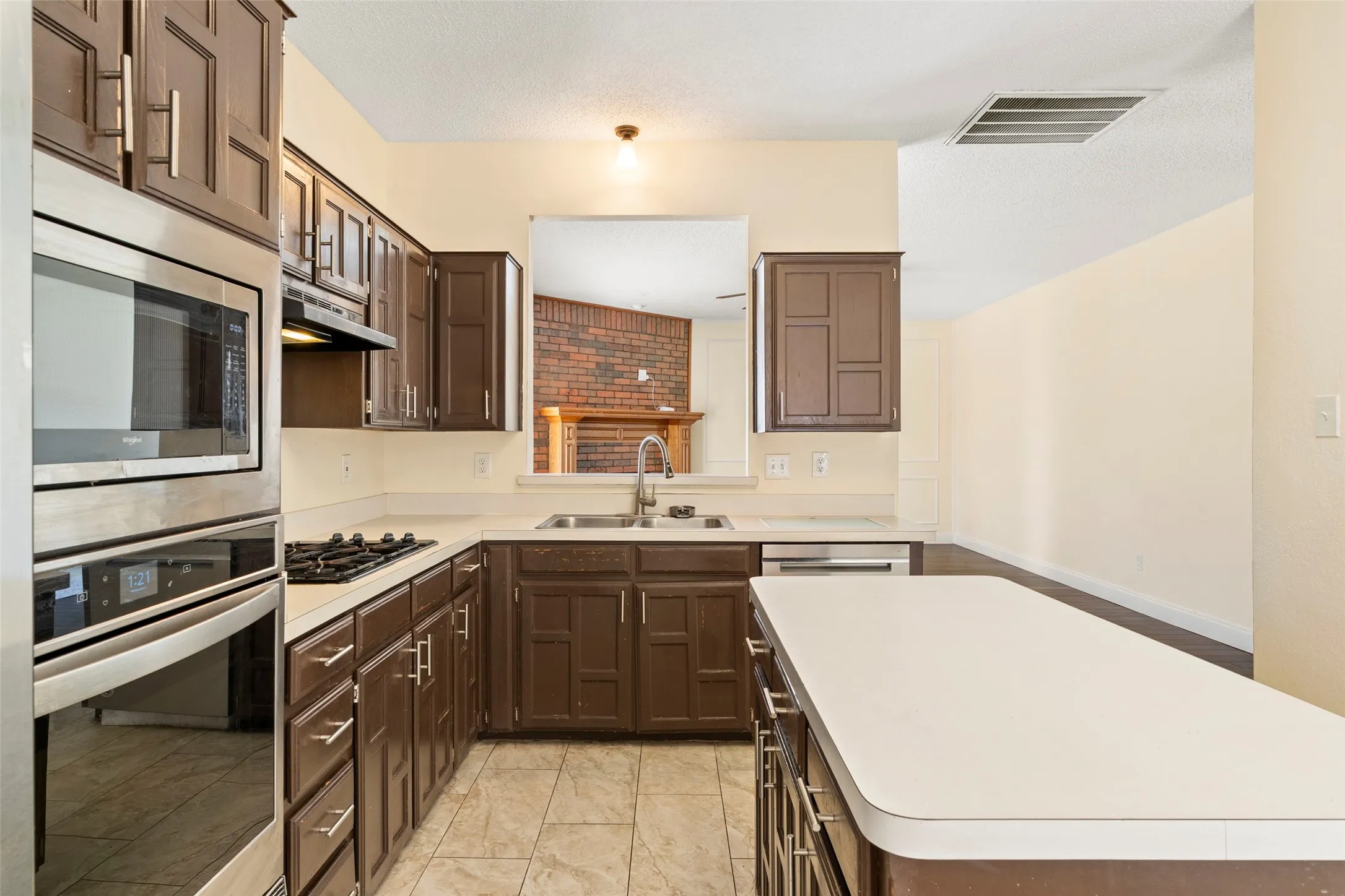 Kitchen featuring dark wood cabinetry, light countertops, stainless steel appliances, a gas cooktop, and tile flooring