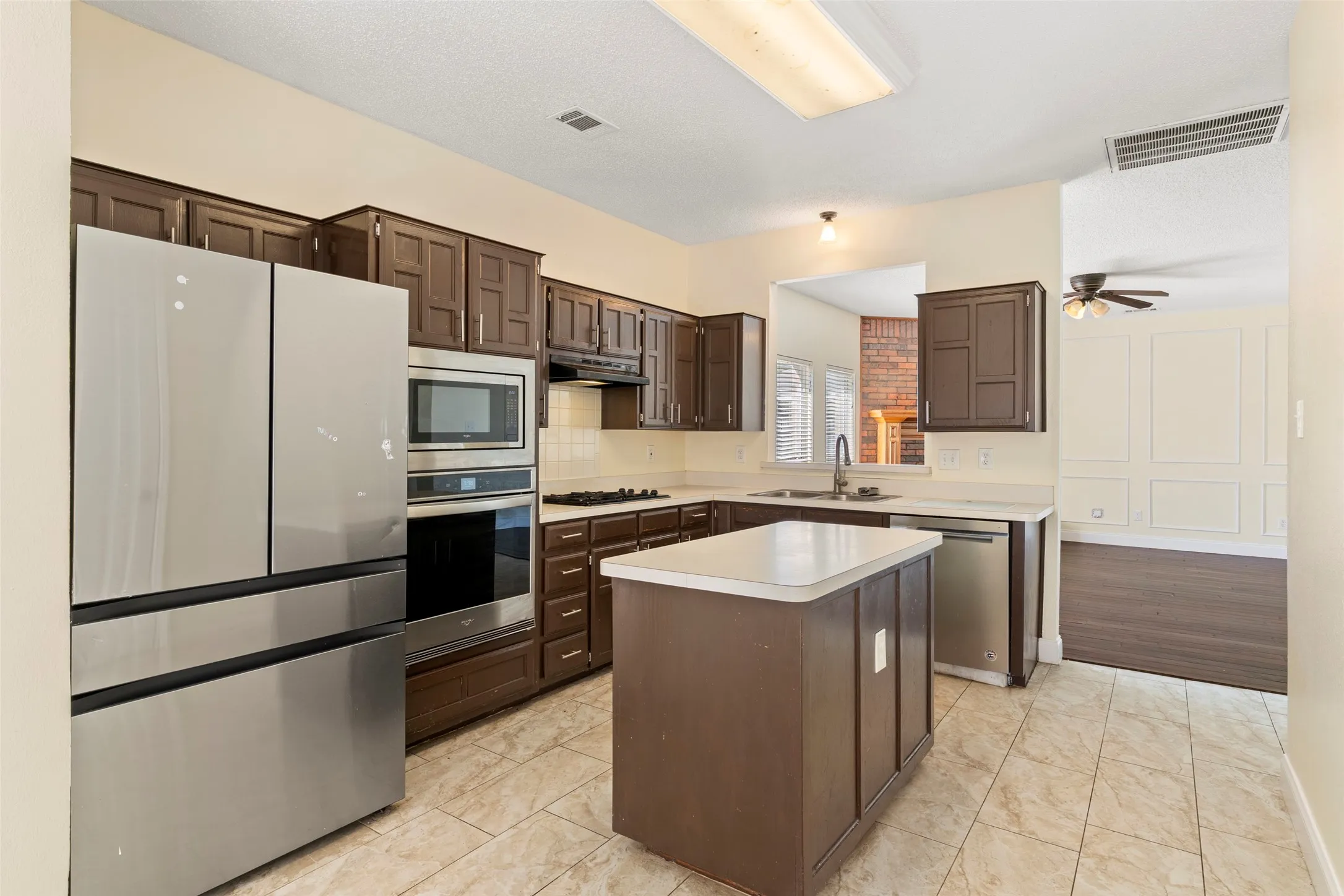 Kitchen featuring an island, tile flooring, dark wood cabinetry, and stainless steel appliances including a built-in oven, microwave, and refrigerator