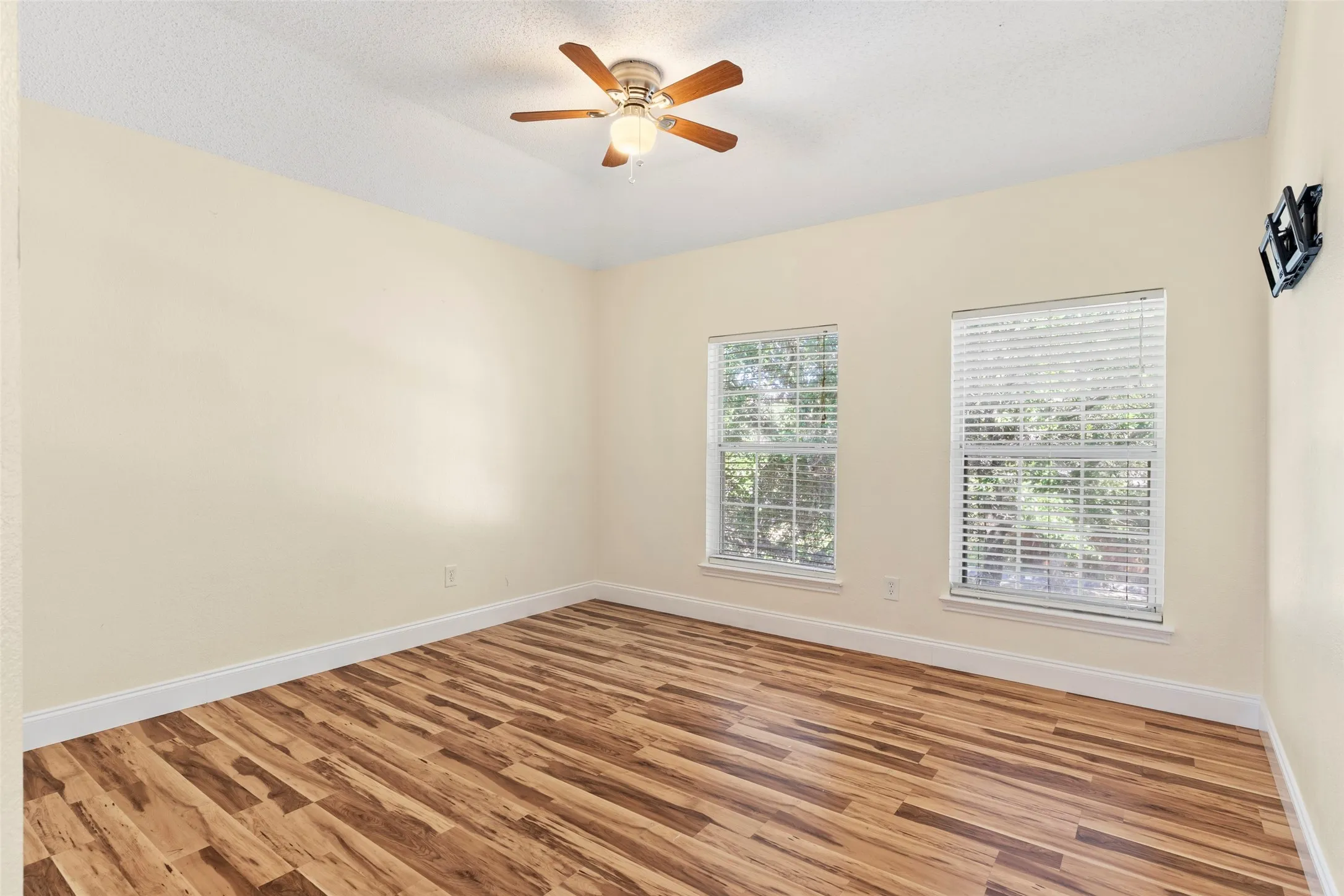 Neutral wall color, wood-finish flooring, two windows with blinds, ceiling fan with integrated lighting, and white baseboards