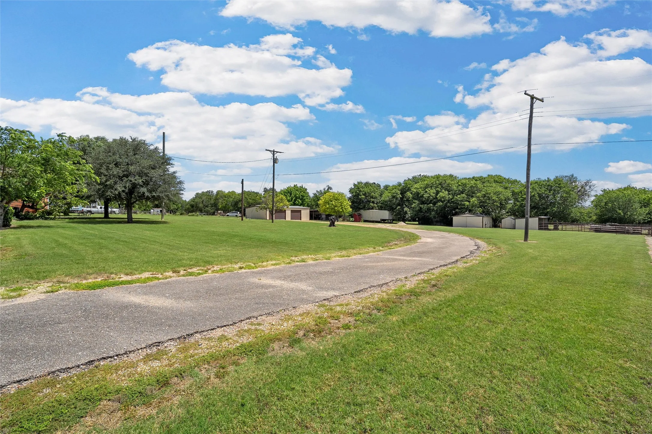 Spacious grounds featuring a paved drive, extensive lawn, mature trees, and multiple outbuildings
