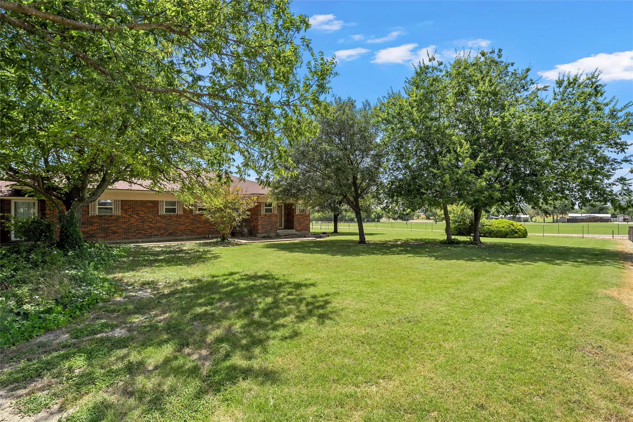 Brick exterior residence featuring a front yard with mature trees, established landscaping, and a manicured lawn
