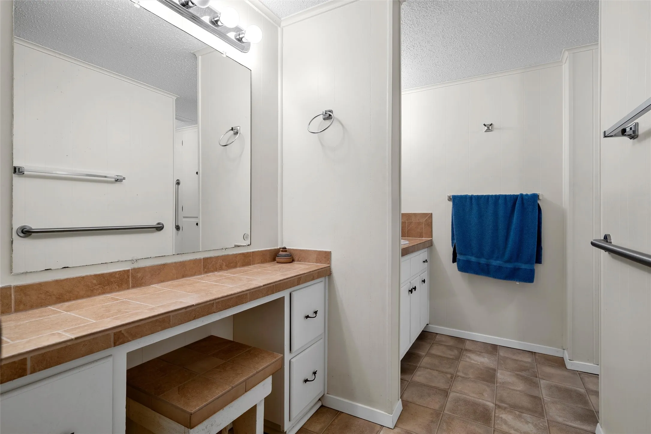 Vanity area featuring a tiled countertop, integrated seating, and a large wall mirror with overhead lighting