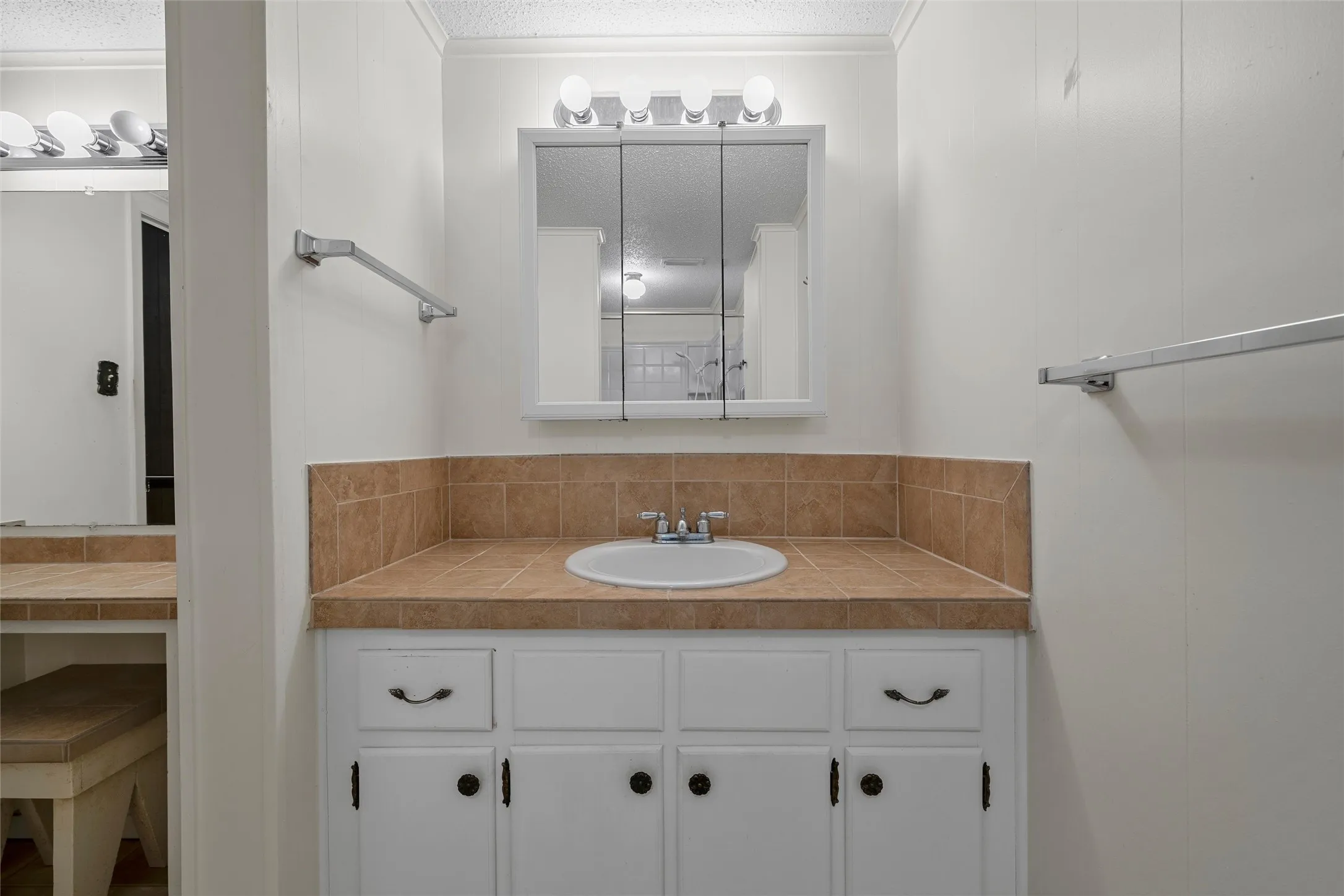 Bathroom vanity featuring a white sink, tile countertop, and medicine cabinet with integrated lighting