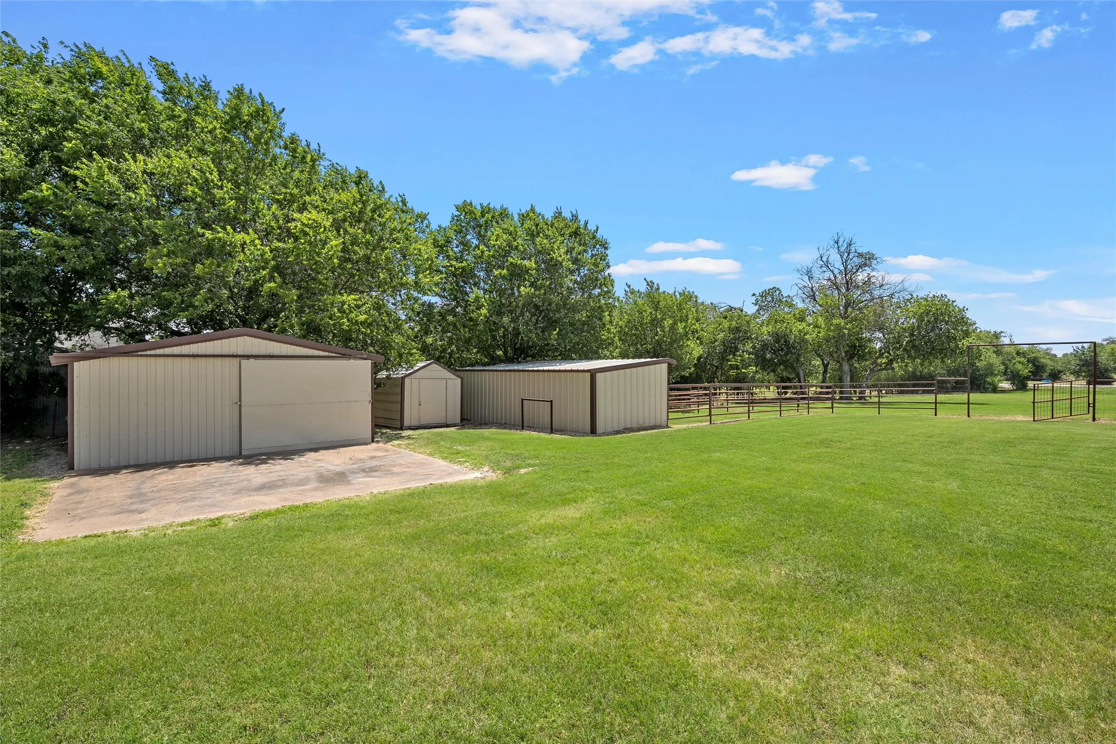 Expansive green space featuring two storage buildings, one utility shed, concrete pad, and perimeter fencing