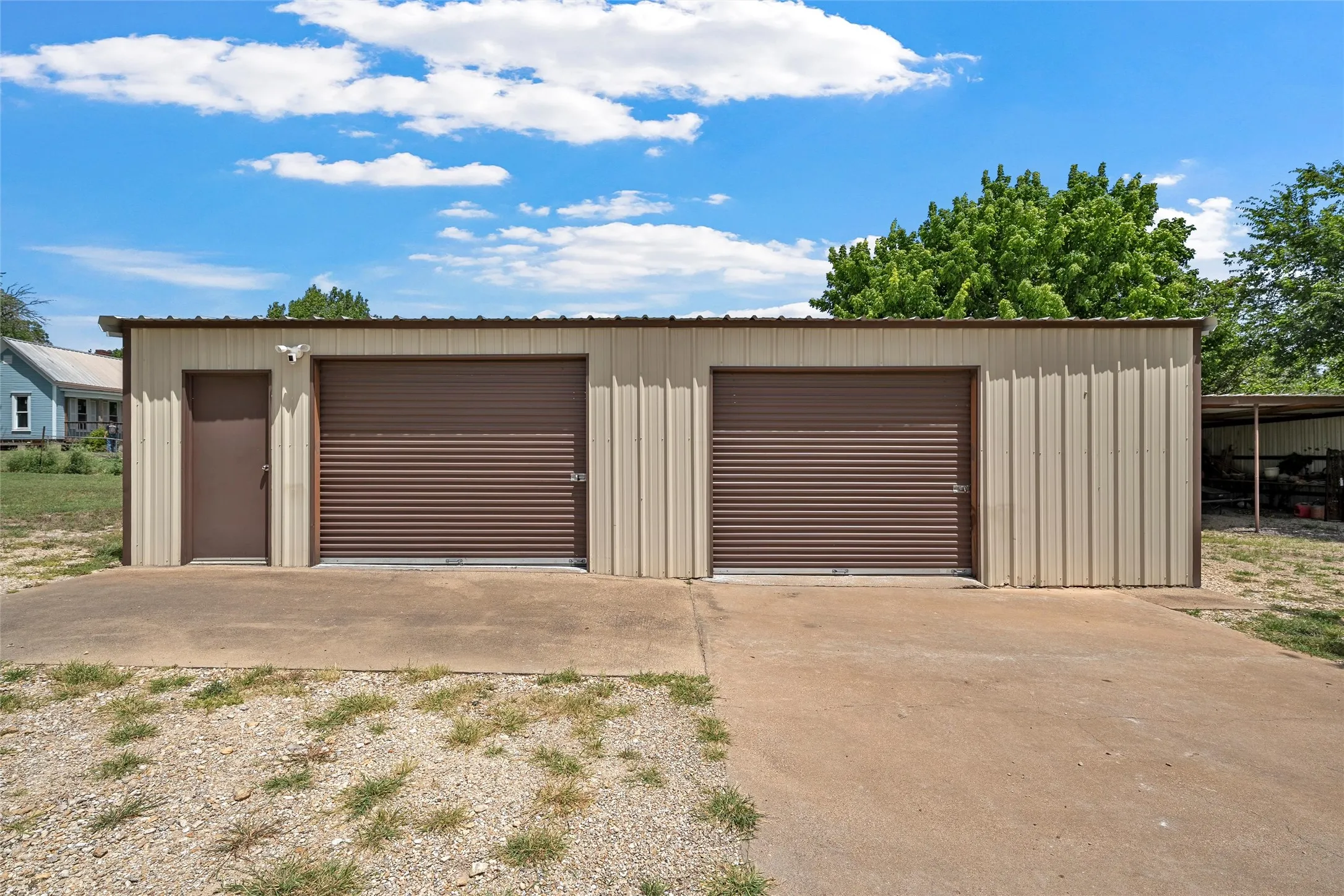 Metal storage building featuring two brown roll-up garage doors, a brown pedestrian door, and a light-colored corrugated metal exterior