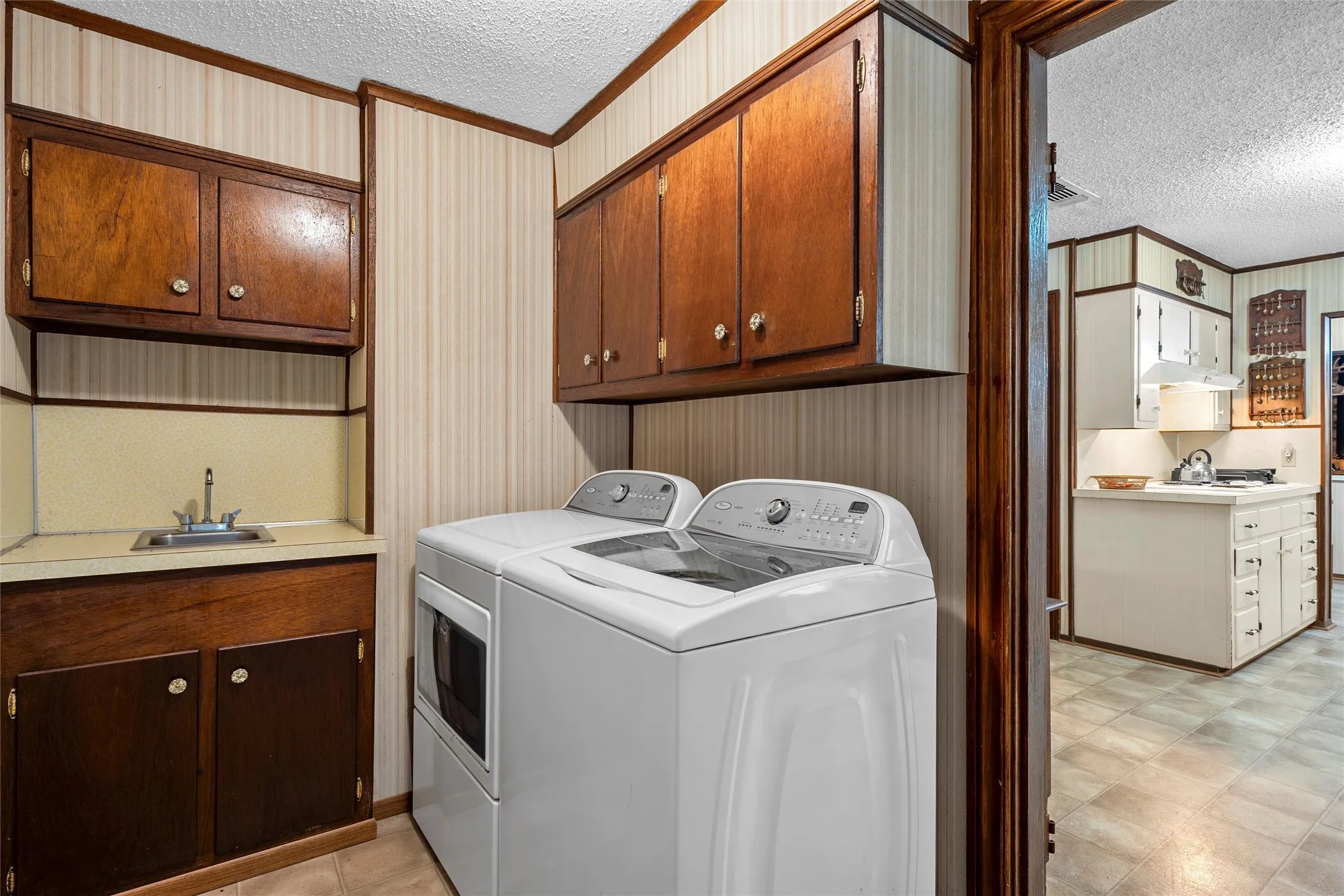 Dedicated laundry area featuring a utility sink, dark wood cabinetry, and neutral-toned wallpaper