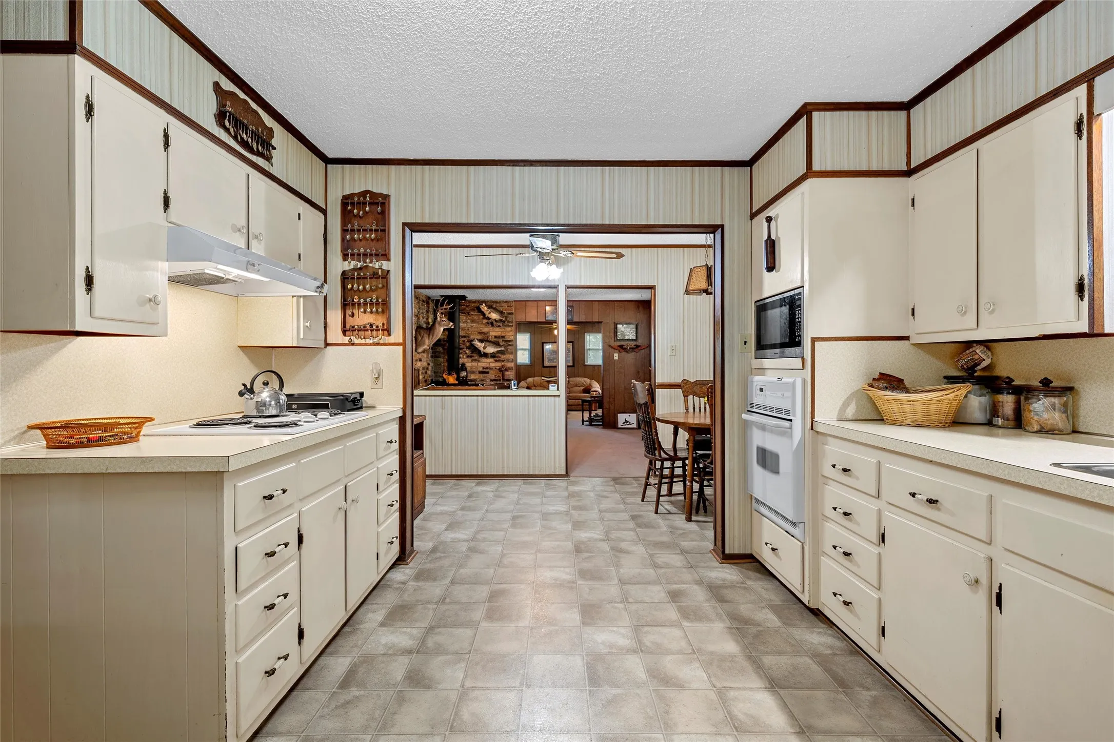 Galley kitchen featuring dual countertops, white cabinetry with dark hardware, built-in wall oven, and microwave