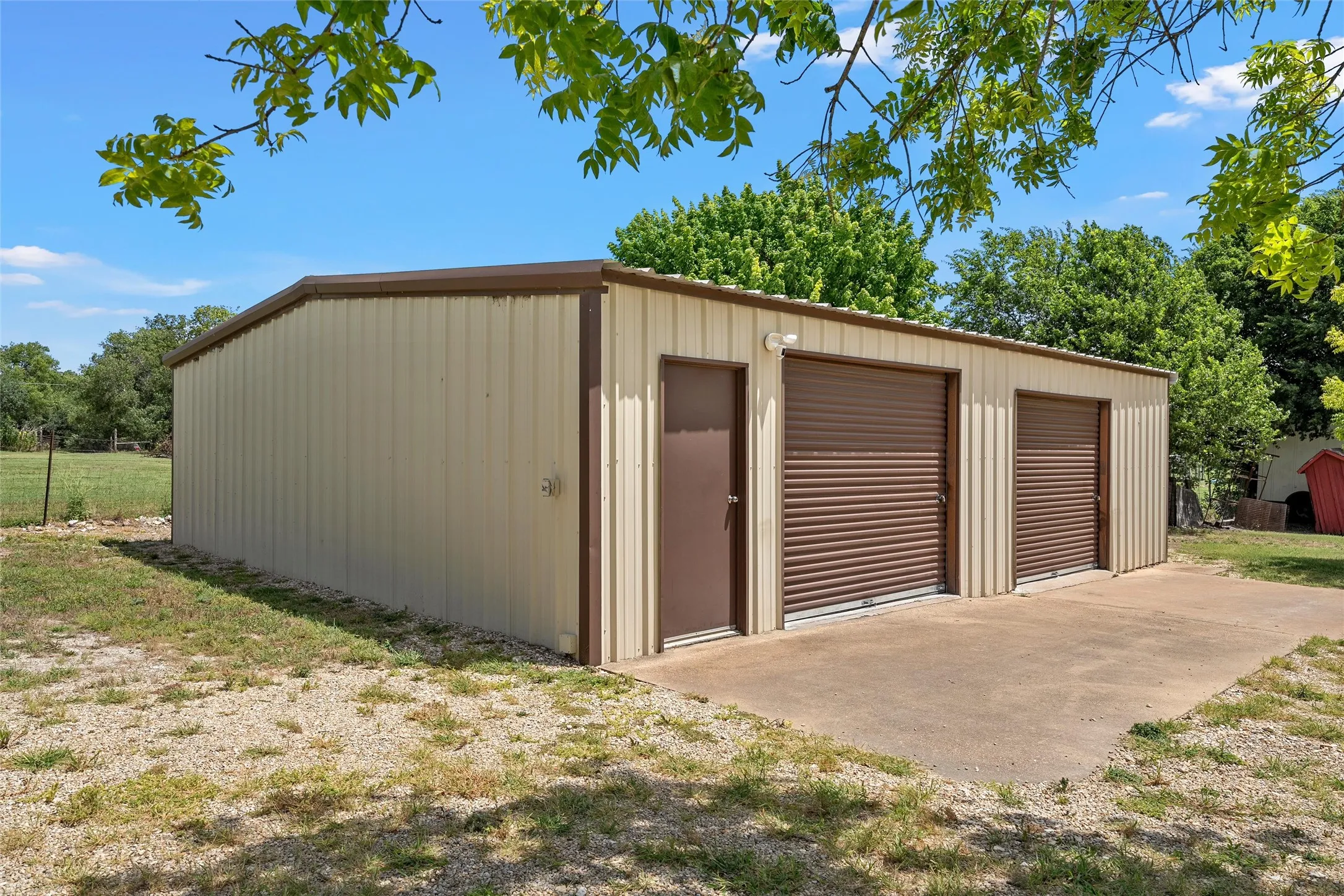 Metal outbuilding with two rollup garage doors, a pedestrian entry door, and exterior lighting