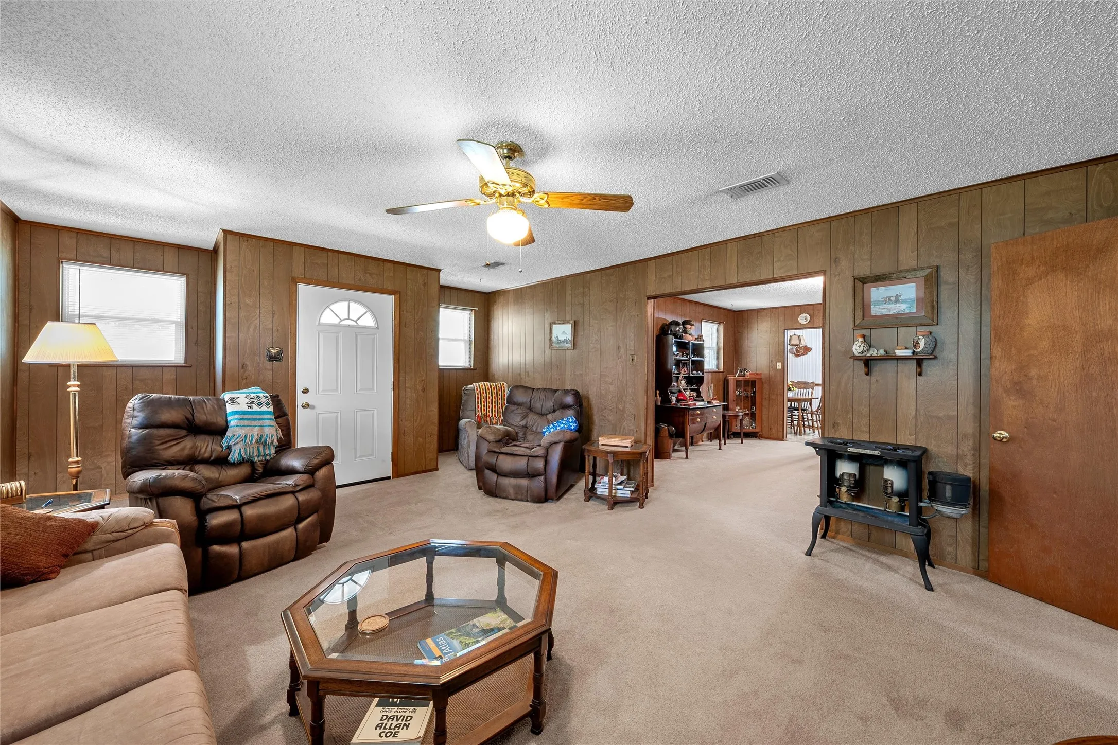 Wood-paneled living area featuring neutral carpeting, a white multi-pane front door, and a ceiling fan with integrated lighting