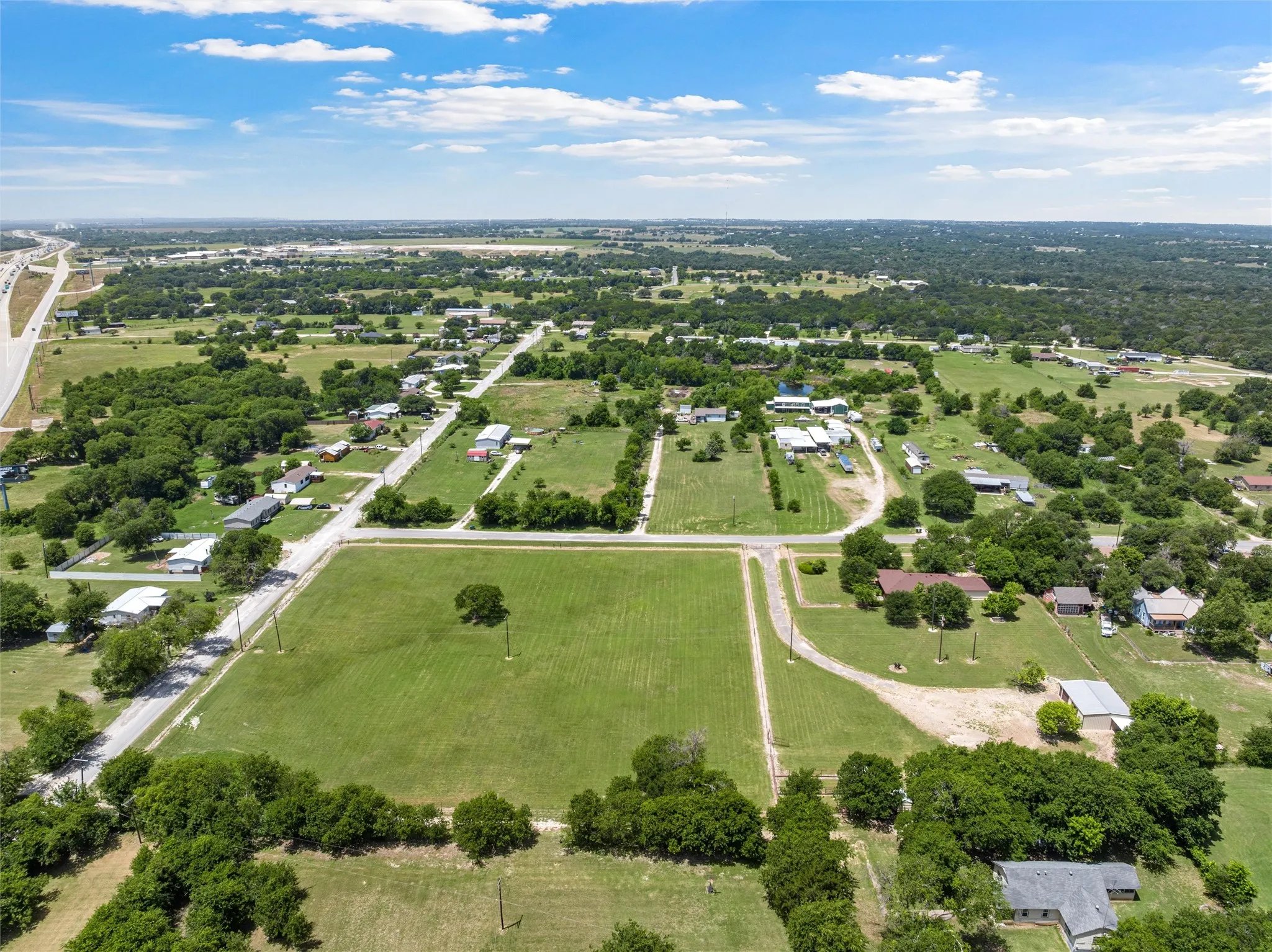 Expansive green landscape with scattered residential properties, mature trees, and a visible highway in the distance