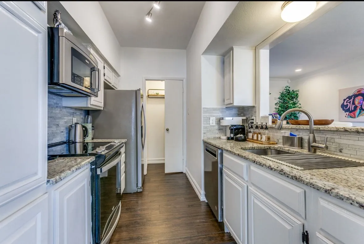 Kitchen with stainless steel appliances, decorative backsplash, light stone countertops, dark wood finished floors, and white cabinets