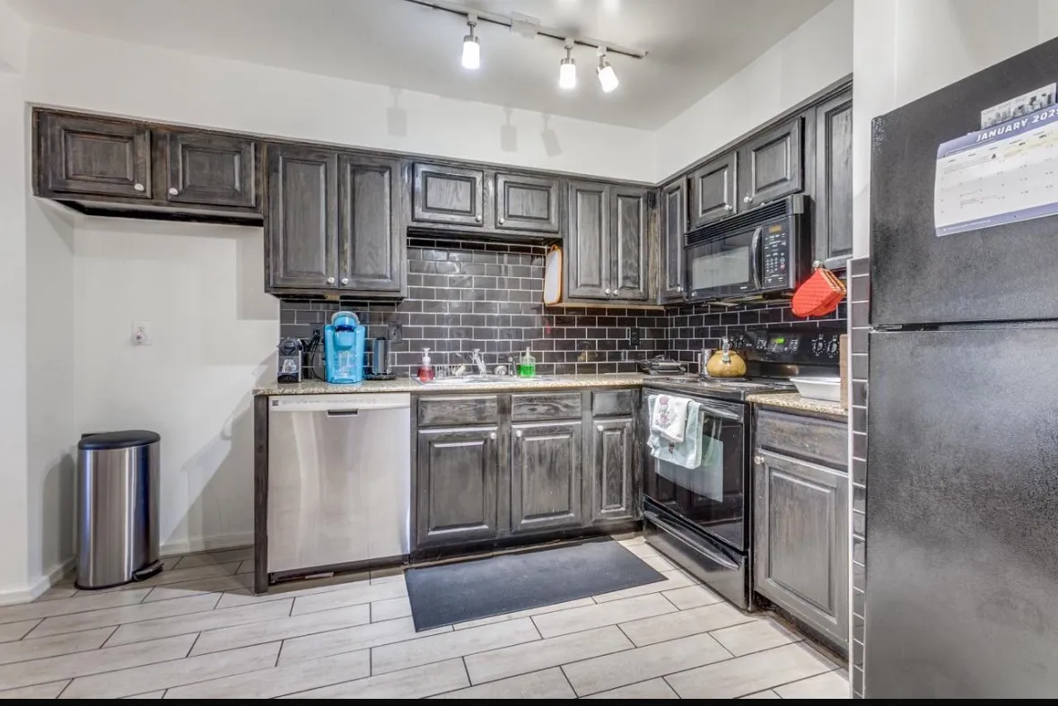 Kitchen with black appliances, tasteful backsplash, wood tiled floors, and light stone counters