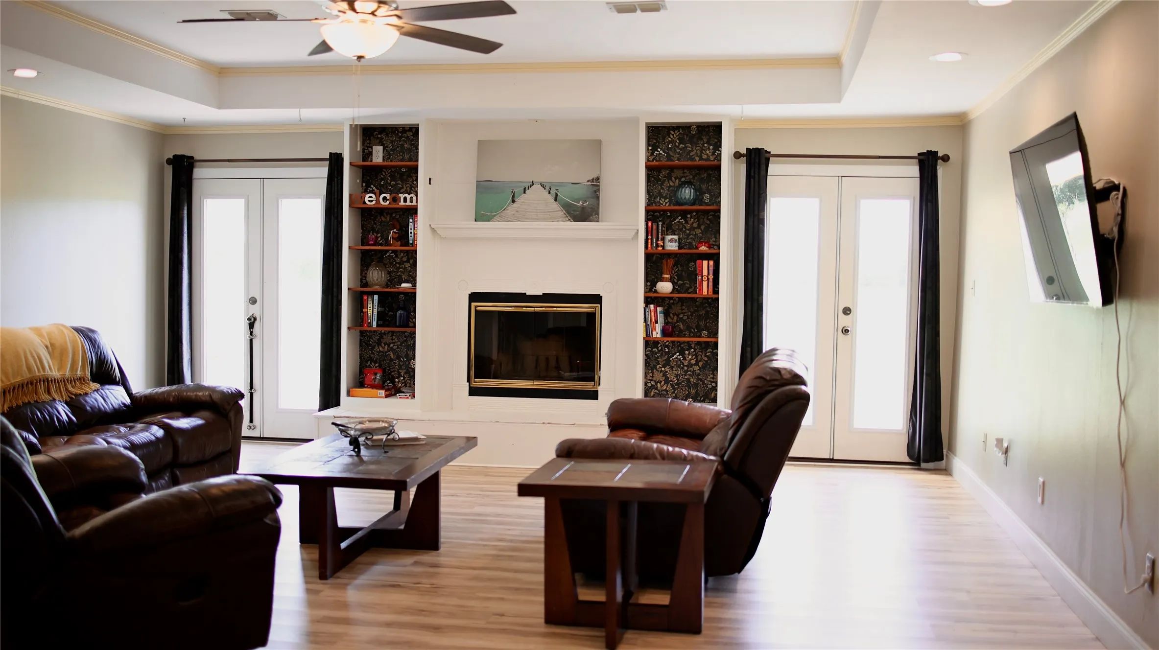 Living area featuring light wood-finish flooring, a tray ceiling with a ceiling fan, and recessed lighting