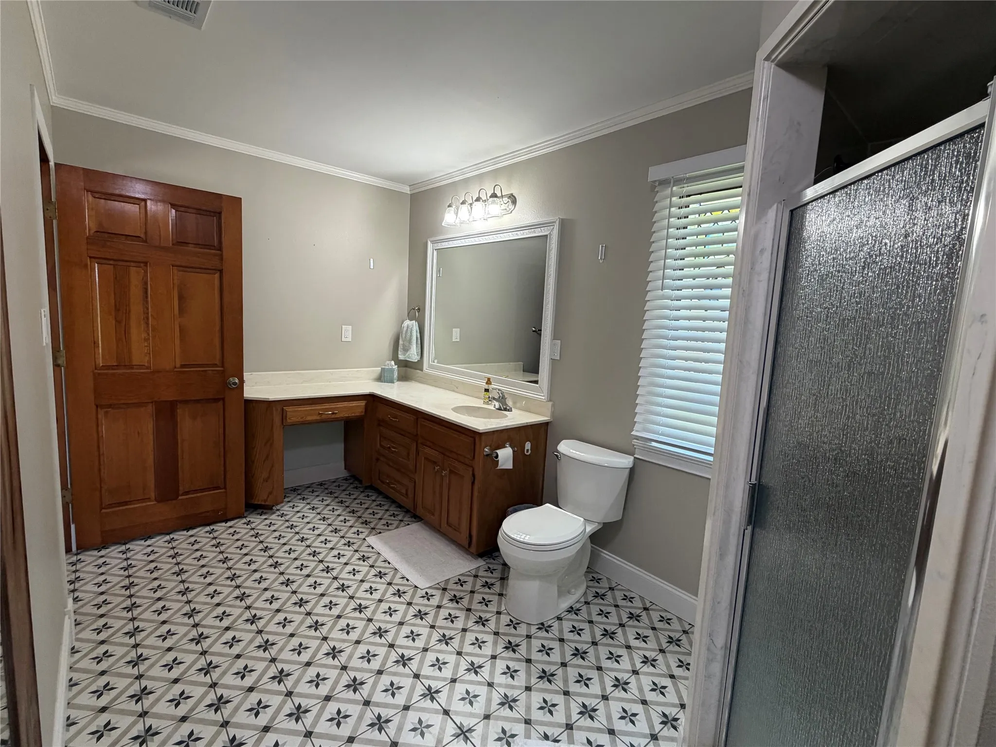 Bathroom featuring geometric pattern floor tiling, a vanity with wood cabinetry and a light-colored countertop, and a shower enclosure with textured glass
