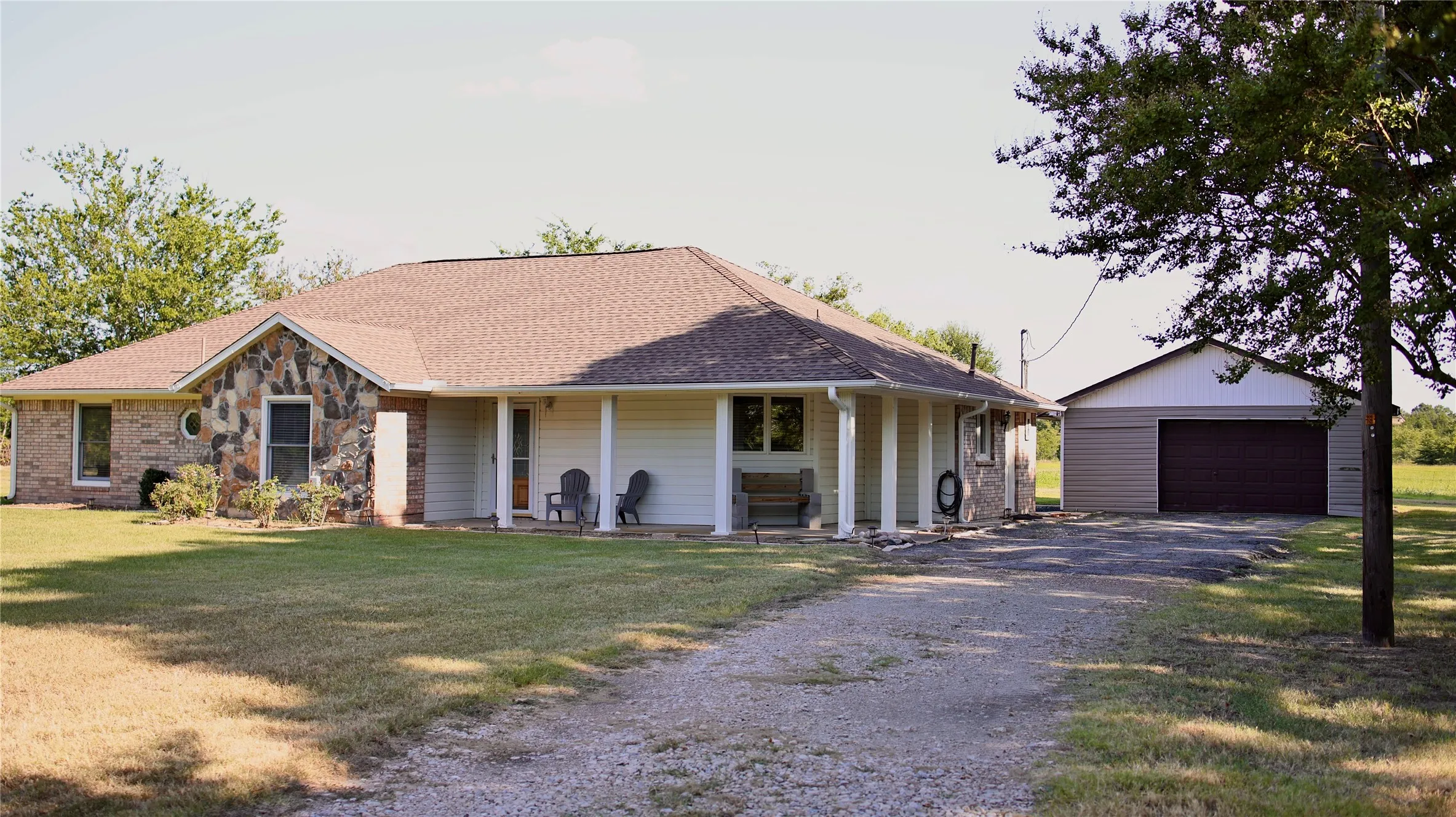 Ranch-style residence featuring a stone and brick facade, a covered front porch with white pillars, and a gravel driveway