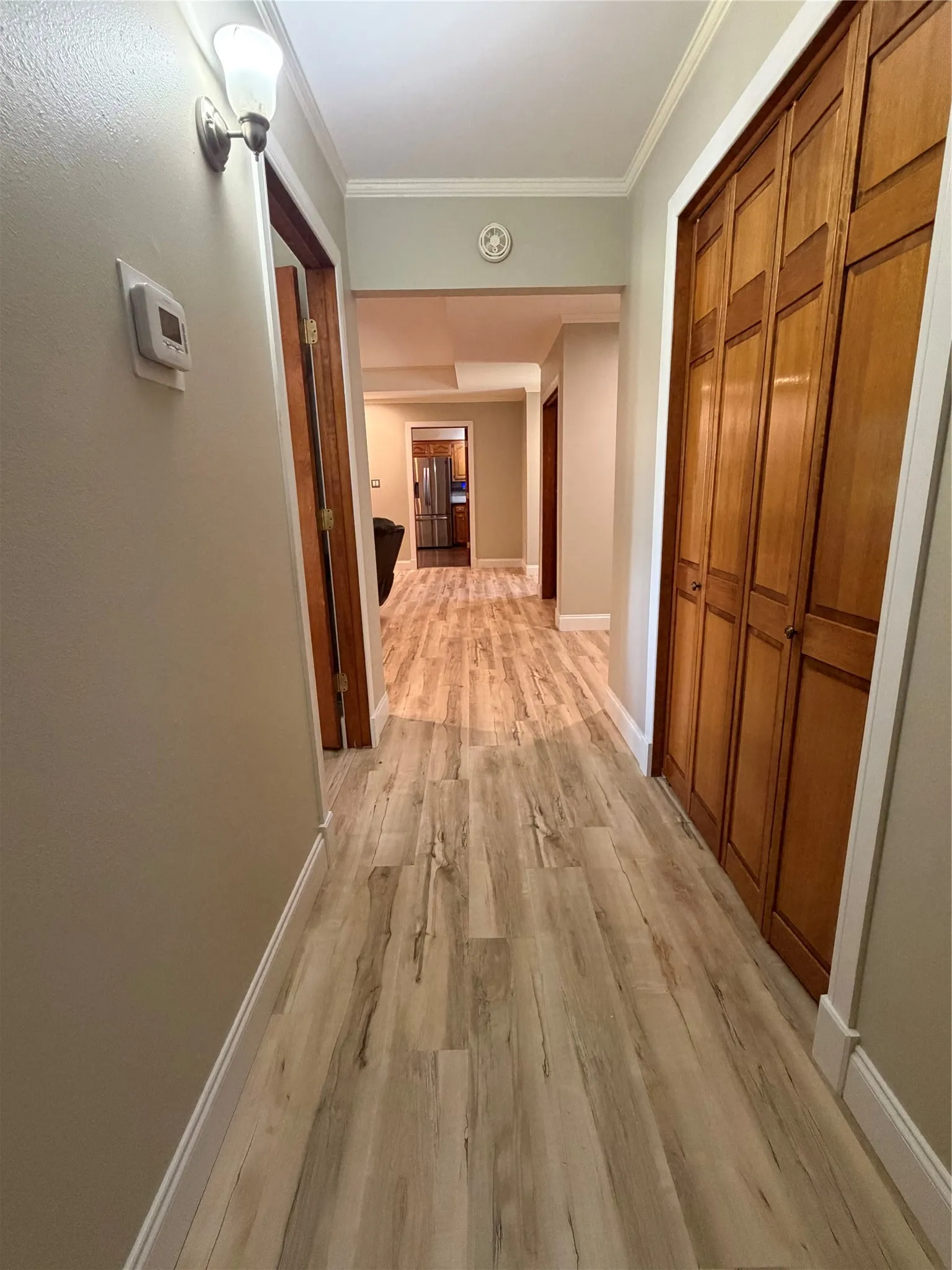 Hallway featuring wood-finish flooring, white crown molding, a built-in light fixture, and wood bi-fold closet doors