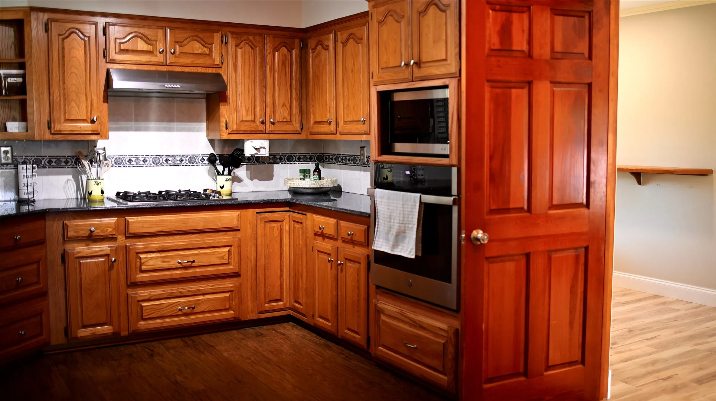 Kitchen featuring wood cabinetry, dark countertops, a tile backsplash, and stainless steel appliances including a built-in oven and microwave