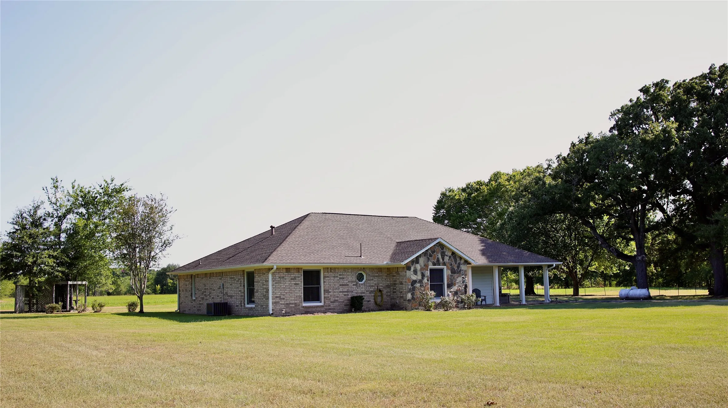Ranch-style residence featuring a combination brick and stone facade, a covered porch, and a shingled roof