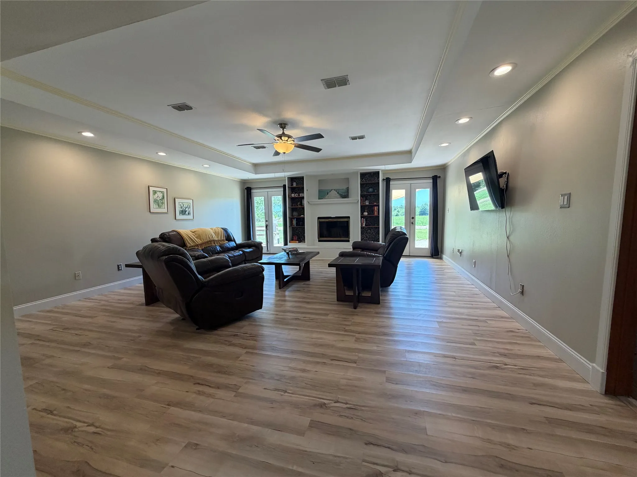 Spacious living area featuring wood-finish flooring, a recessed tray ceiling with recessed lighting, and a ceiling fan