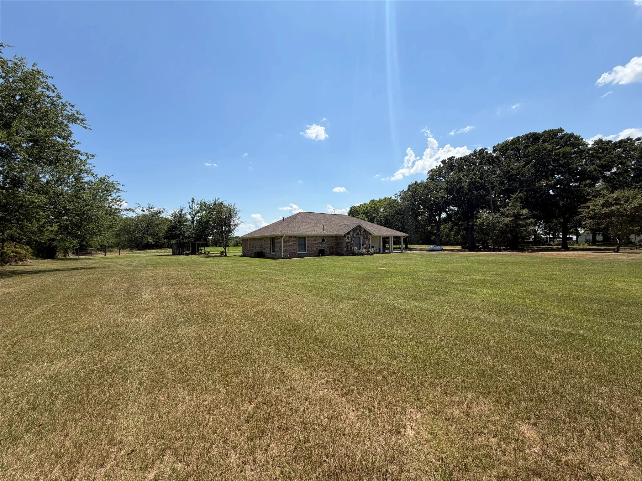 Expansive lawn surrounding a single-story brick exterior residence with a covered patio
