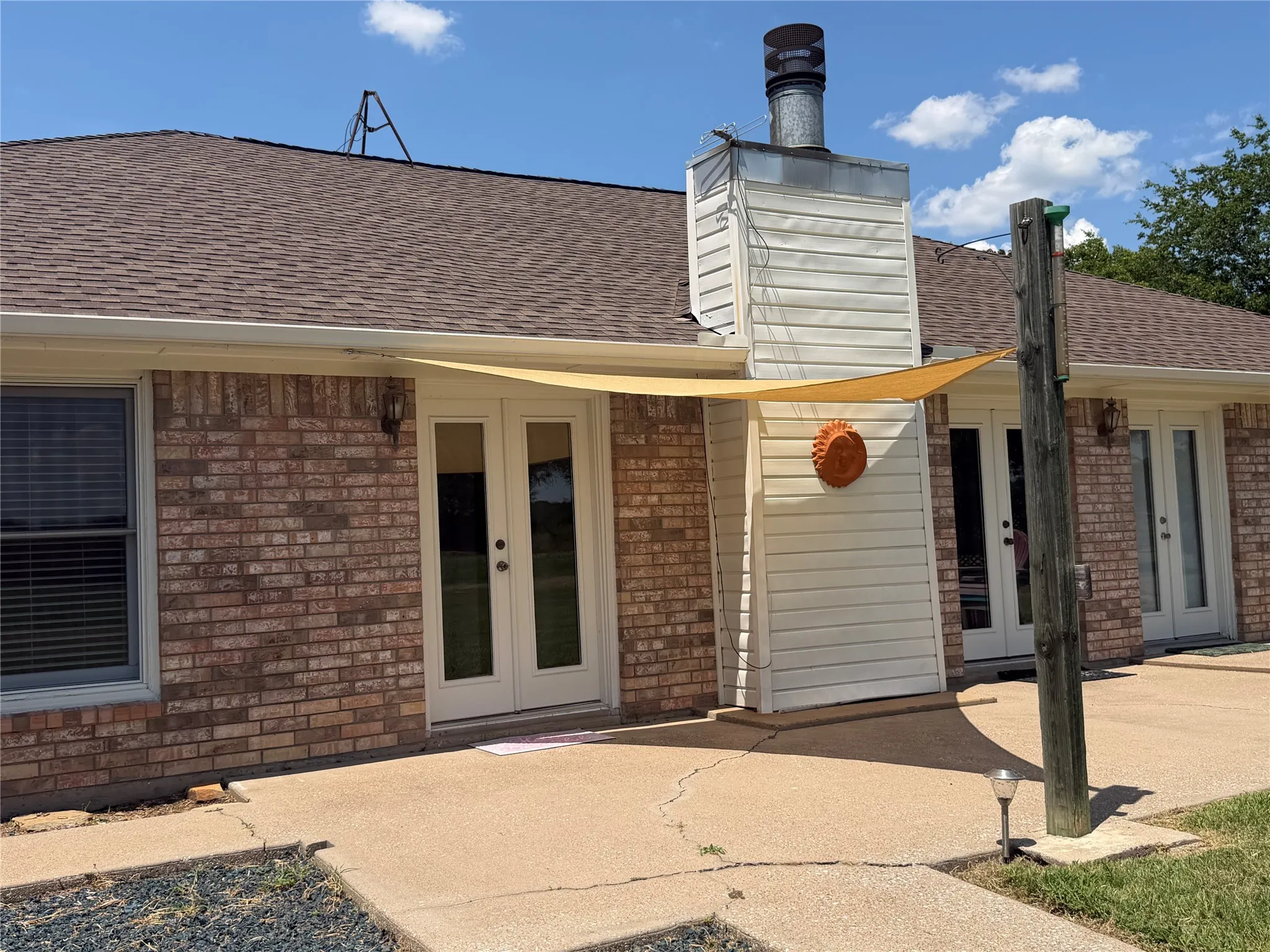 Brick exterior featuring a chimney with metal flue, brown shingle roof, and white rain gutters