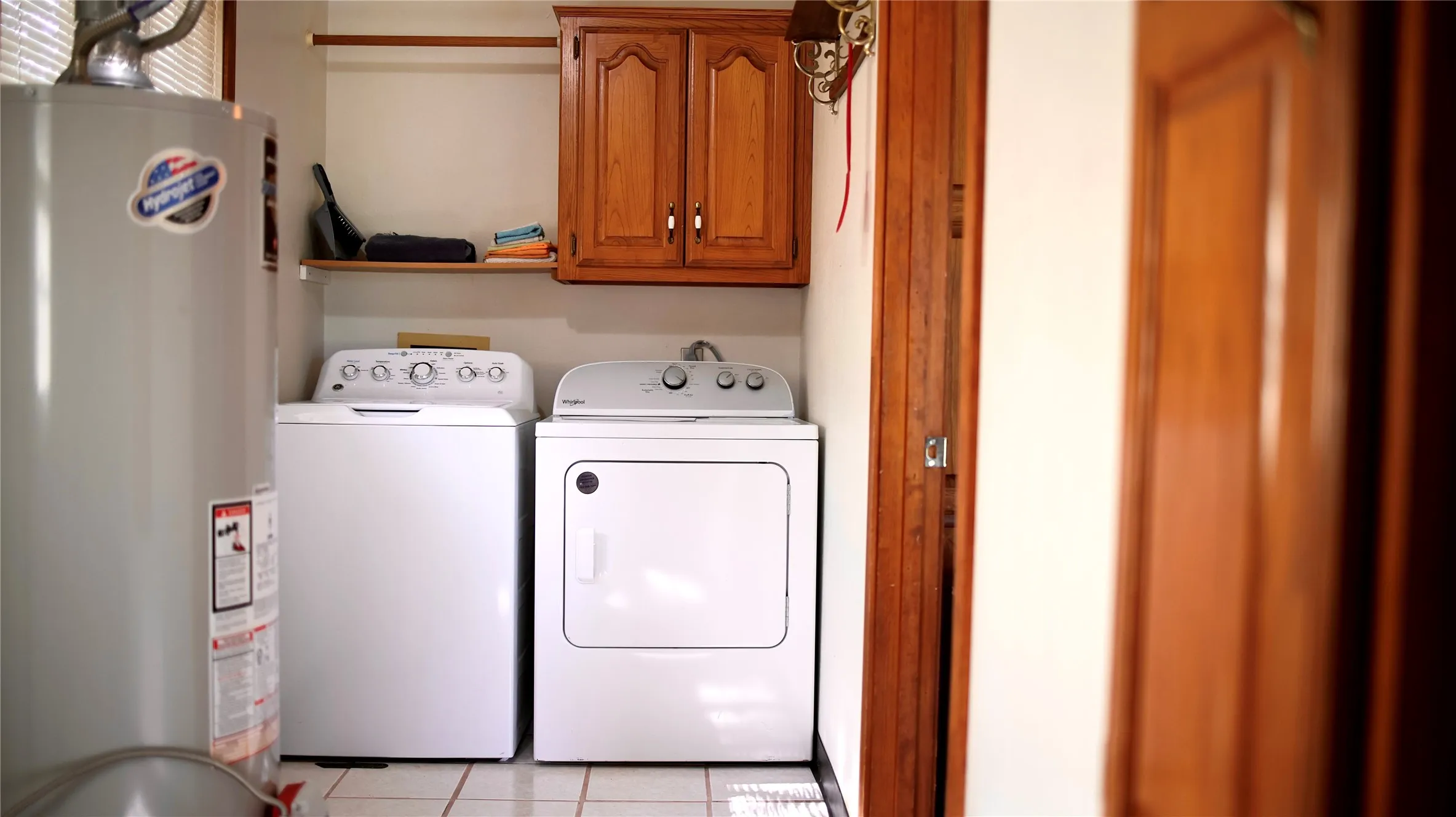 Dedicated laundry area featuring white appliances, a light wood-finish storage cabinet, and a tiled floor