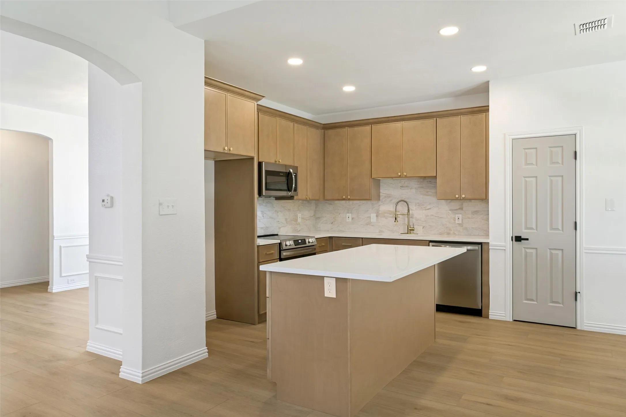 Modern kitchen featuring a central island with a light countertop, wood-finish cabinetry, stainless steel appliances, and a tiled backsplash
