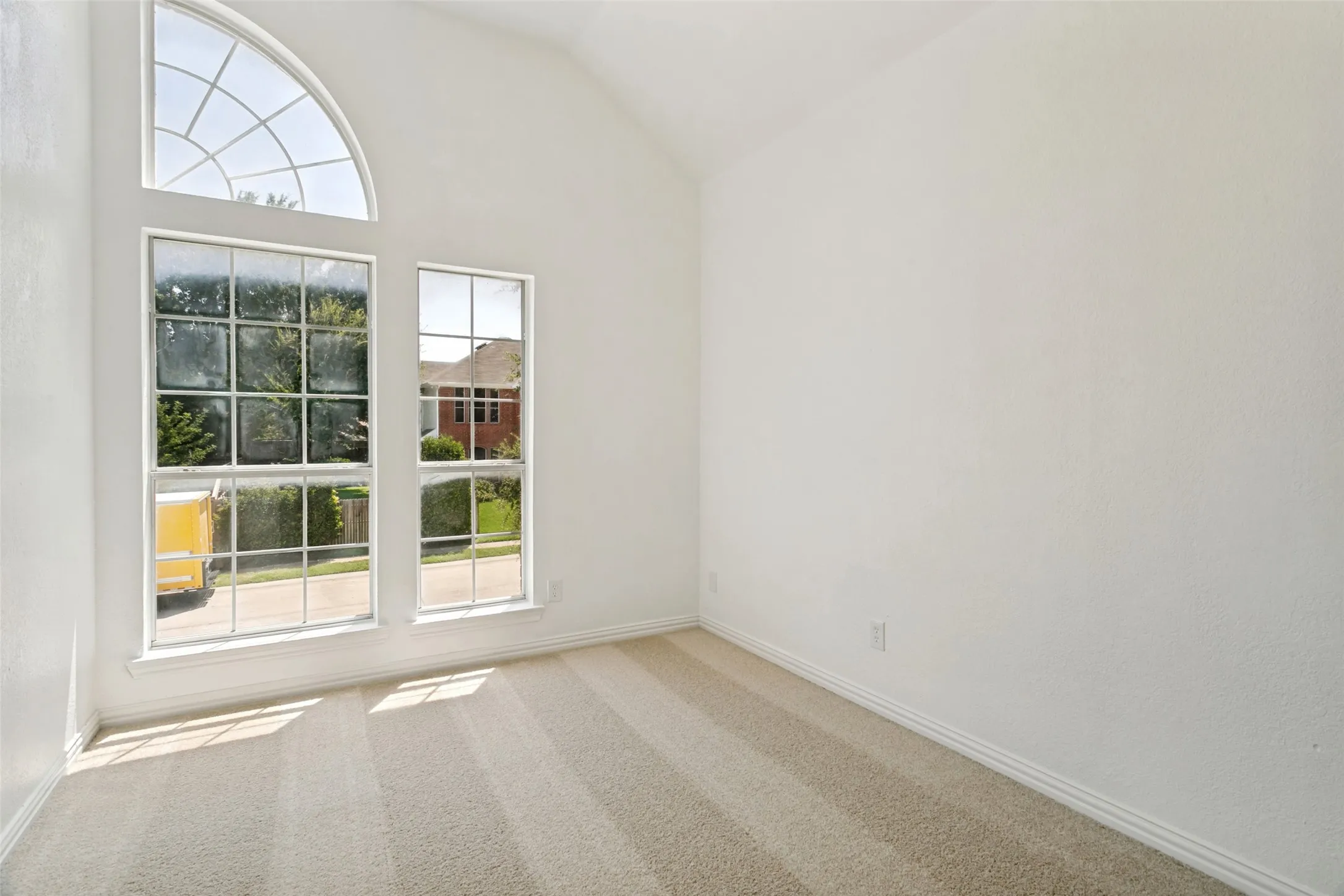 Vaulted ceiling room featuring an arched transom window and two large rectangular windows, providing abundant natural illumination