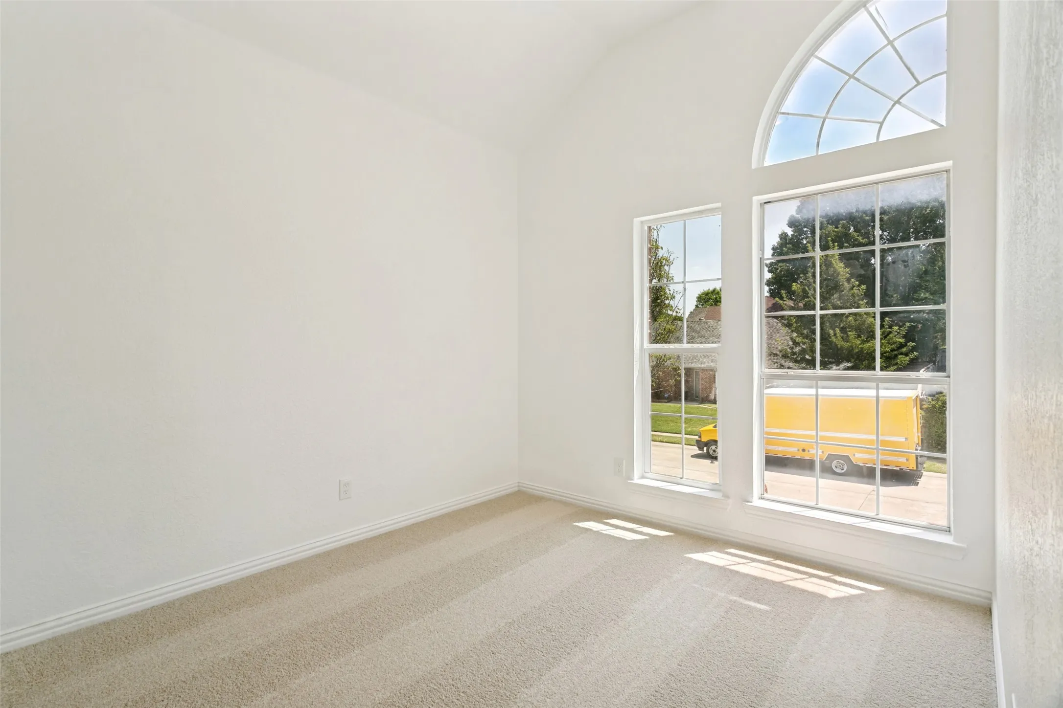 Room with vaulted ceiling, arched transom window, two large rectangular windows, neutral carpet, and white baseboards