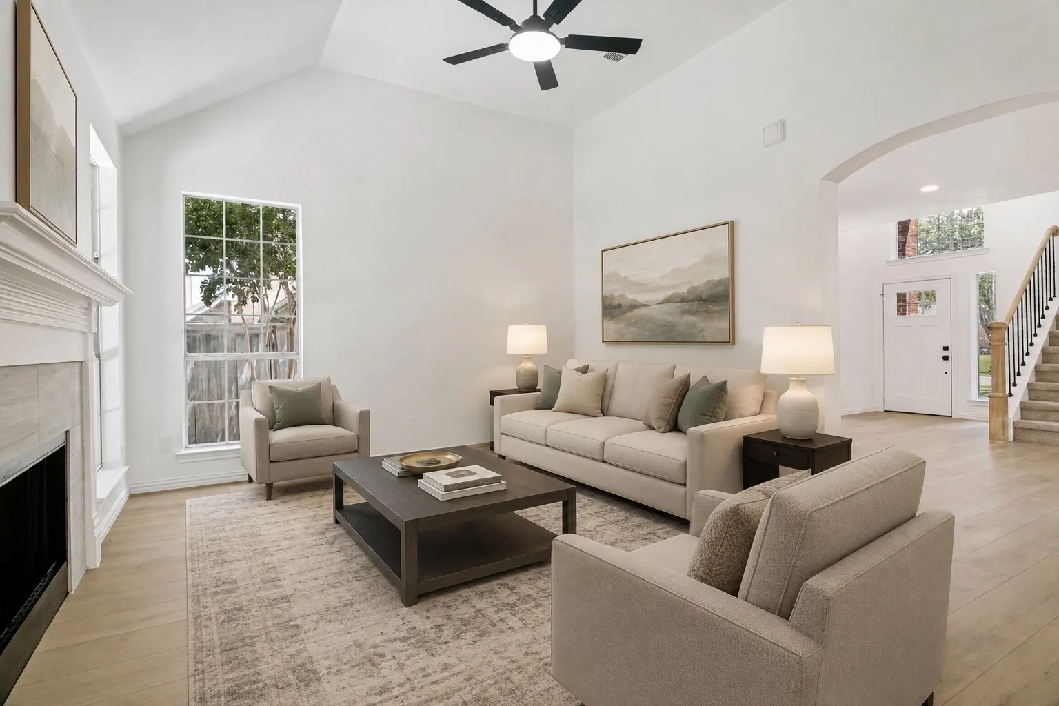 Vaulted ceilings and light wood-finish flooring define this living space, featuring a fireplace with a white mantel and a large window