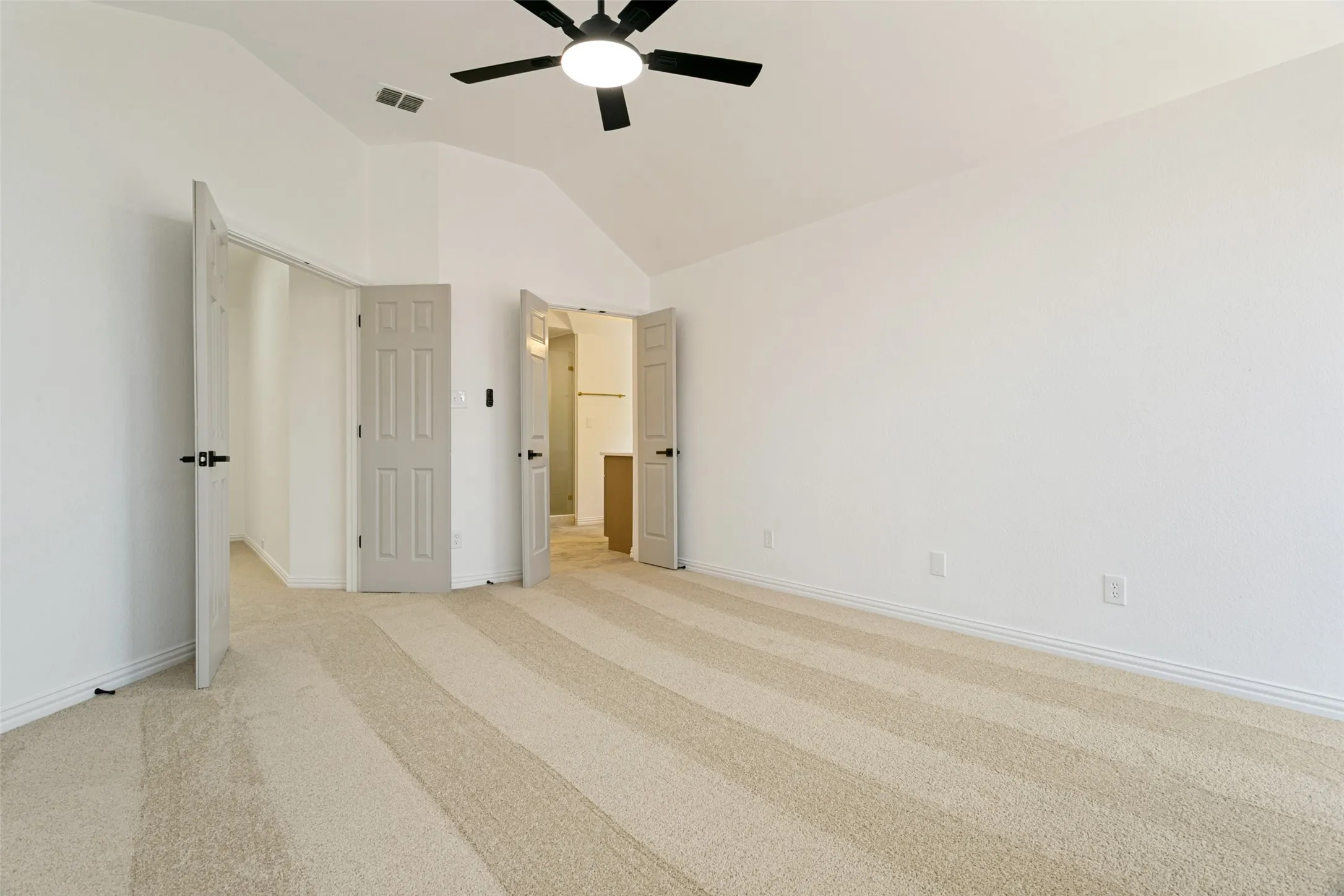 Spacious room featuring vaulted ceilings, a contemporary ceiling fan, light-toned striped carpeting, and multiple panel doors with dark hardware