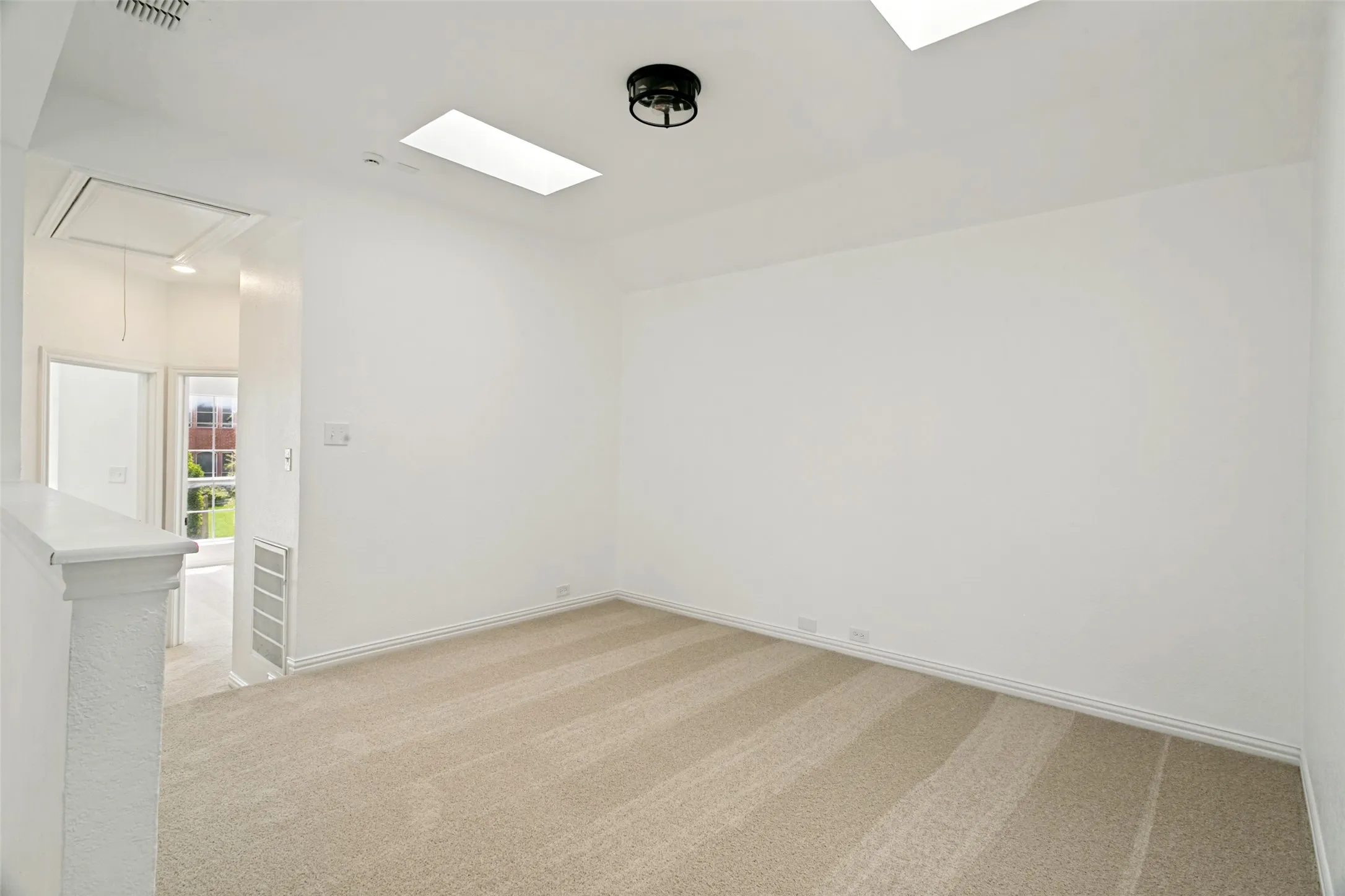 Carpeted room featuring a ceiling-mounted light fixture, two skylights, and white baseboards