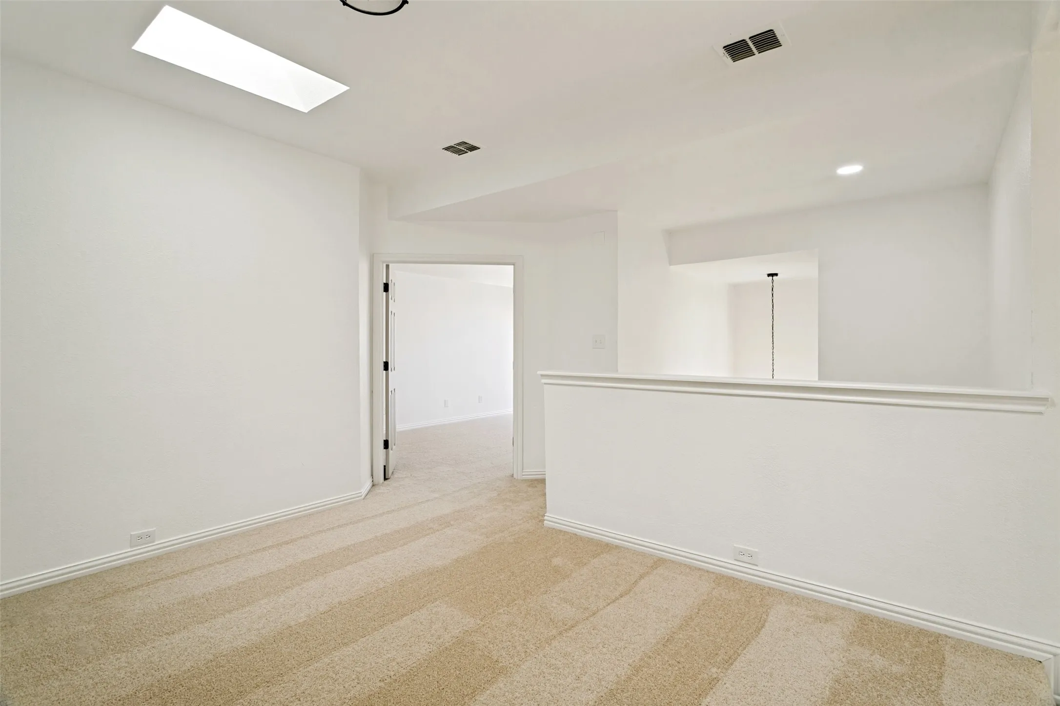 Carpeted landing area featuring a skylight, recessed lighting, white baseboards, and a half-wall partition