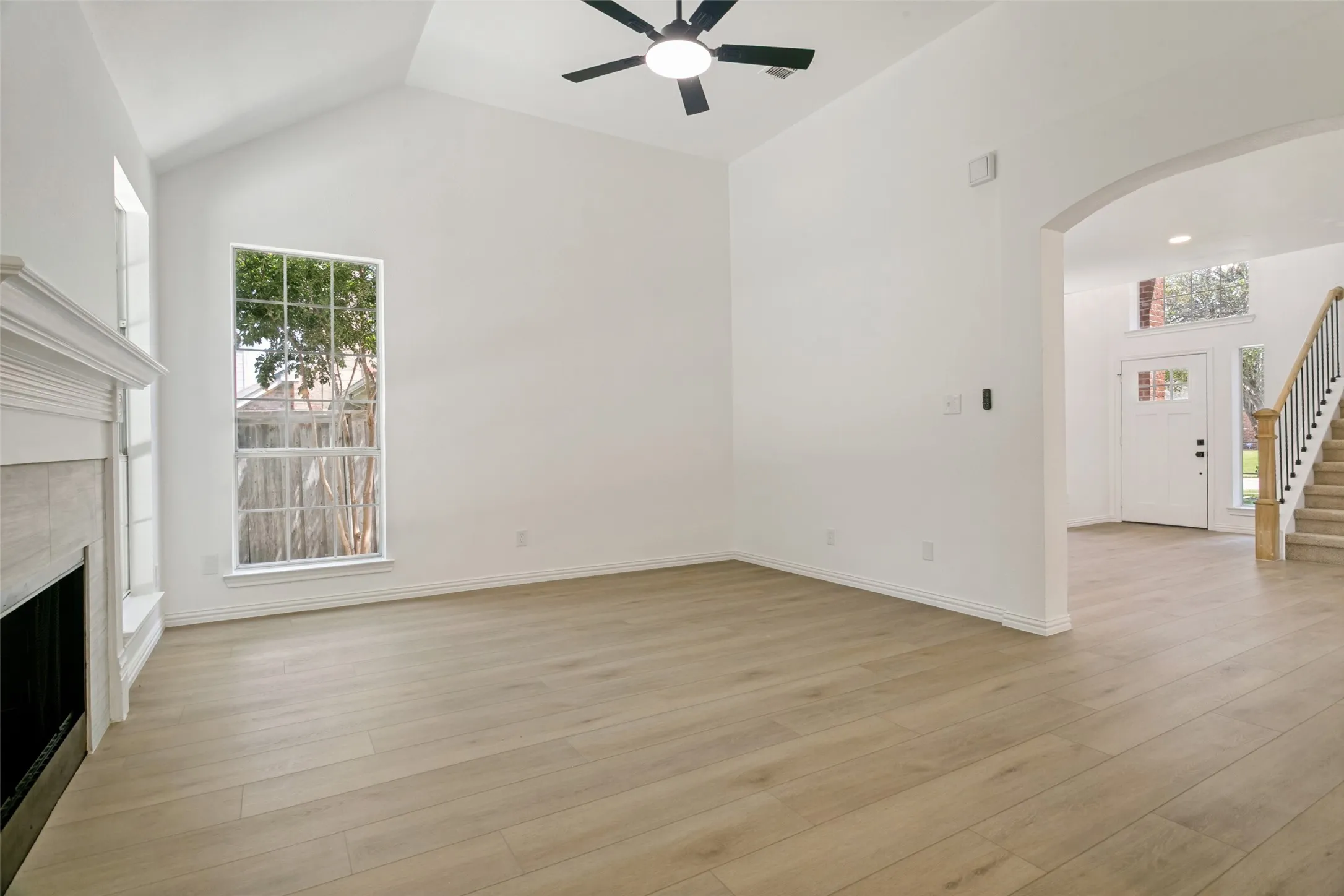 Living area featuring vaulted ceilings, wood-finish flooring, a fireplace with a white mantel, and a ceiling fan