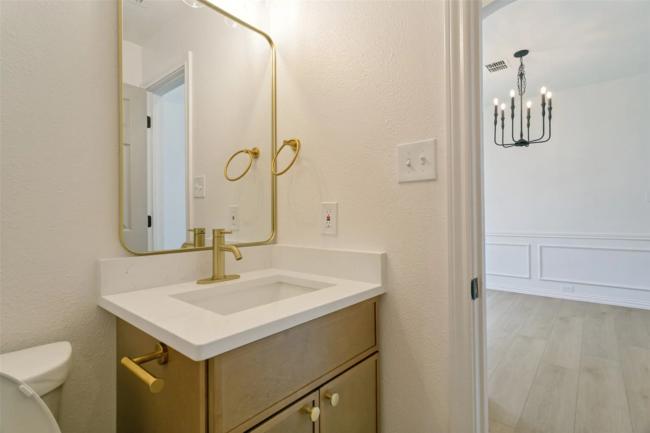 Bathroom vanity with a gold-framed rectangular mirror, matching gold faucet, and a white countertop with an integrated sink