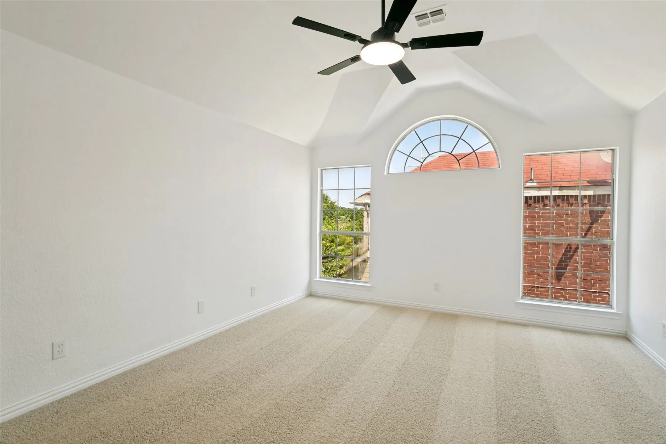 Bright room featuring vaulted ceilings with a ceiling fan, three windows including a large arched window, and neutral-toned carpeting