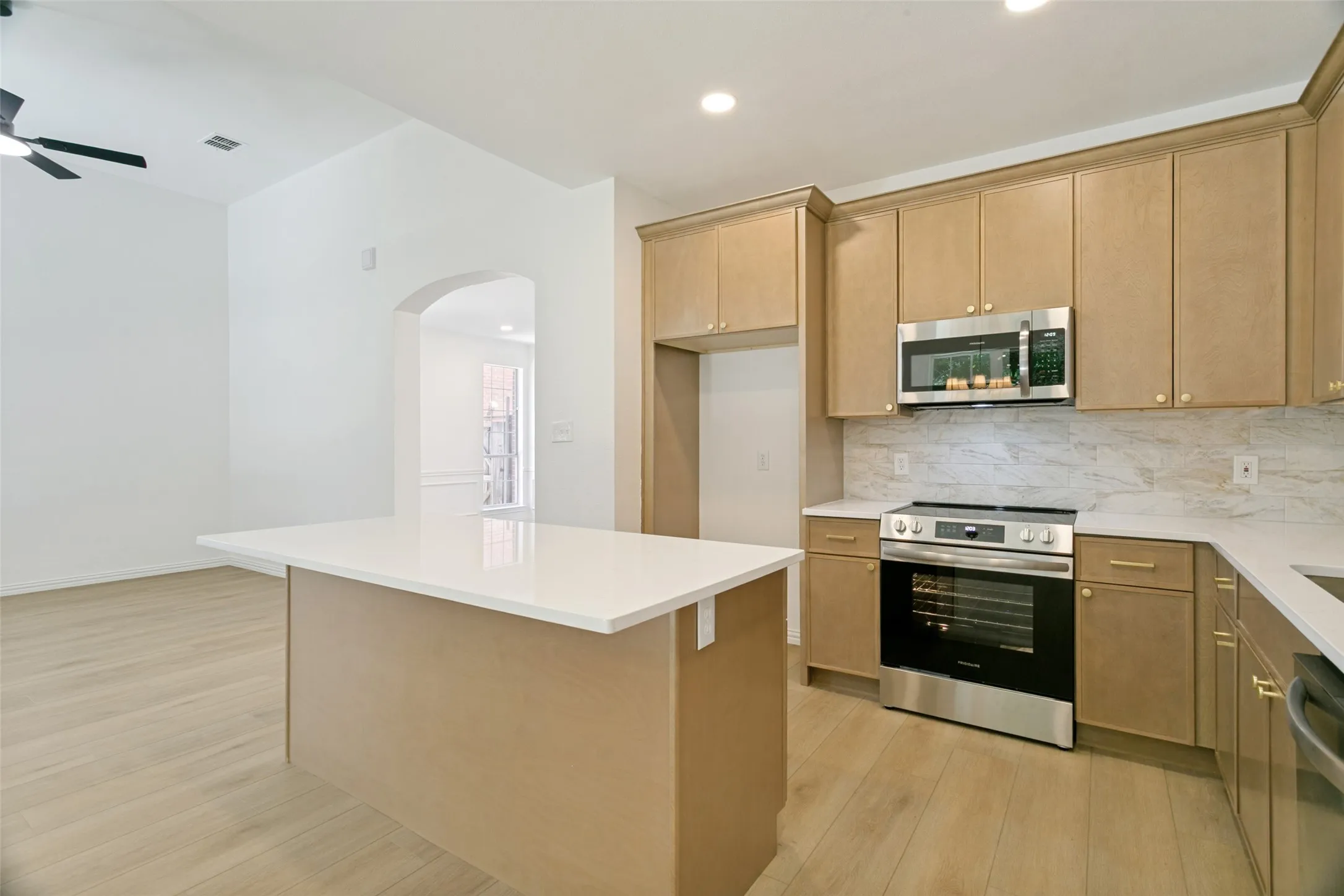 Contemporary kitchen featuring light wood-finish cabinetry, stainless steel appliances, a white countertop island, and wood-finish flooring