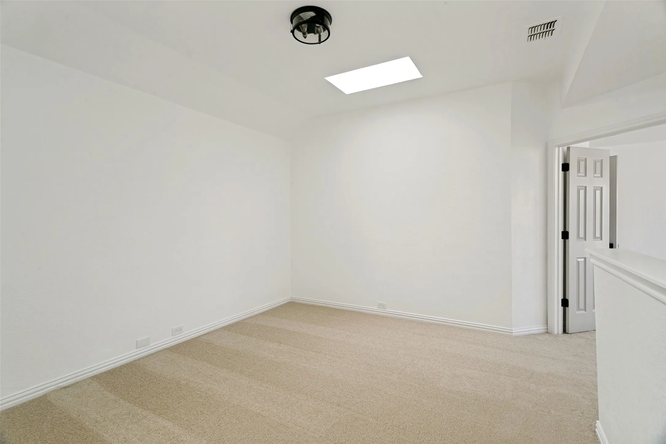 Bright interior space featuring light-toned carpeting, white baseboards, and a skylight