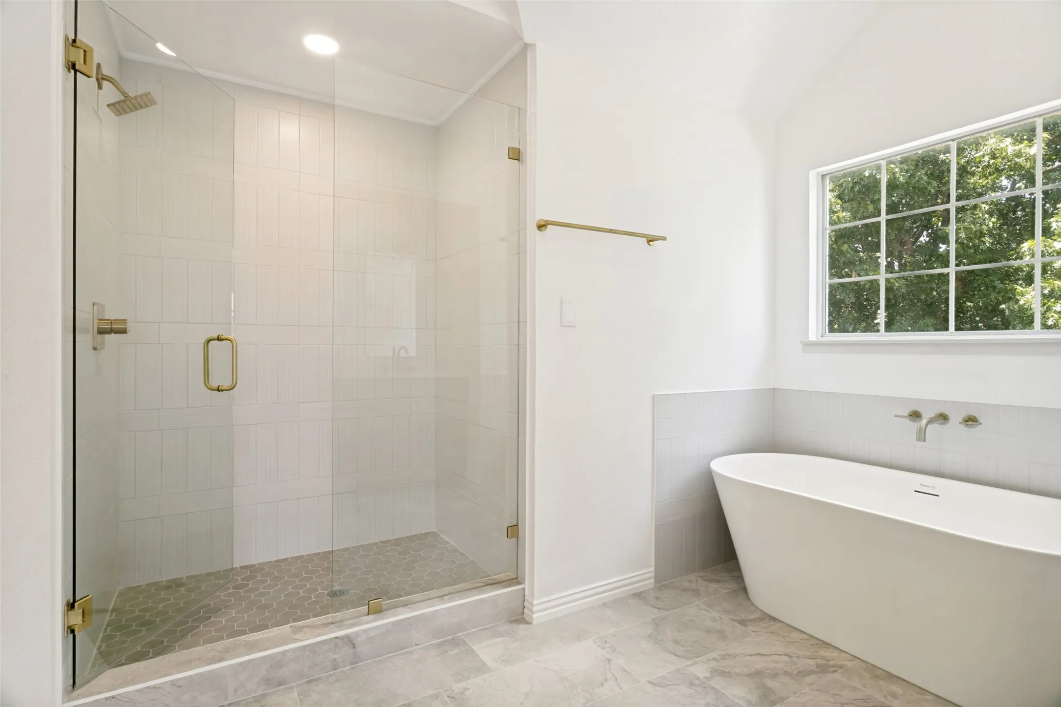 Contemporary bathroom featuring a frameless glass shower enclosure with brass hardware, a freestanding soaking tub, and a window with grid pattern