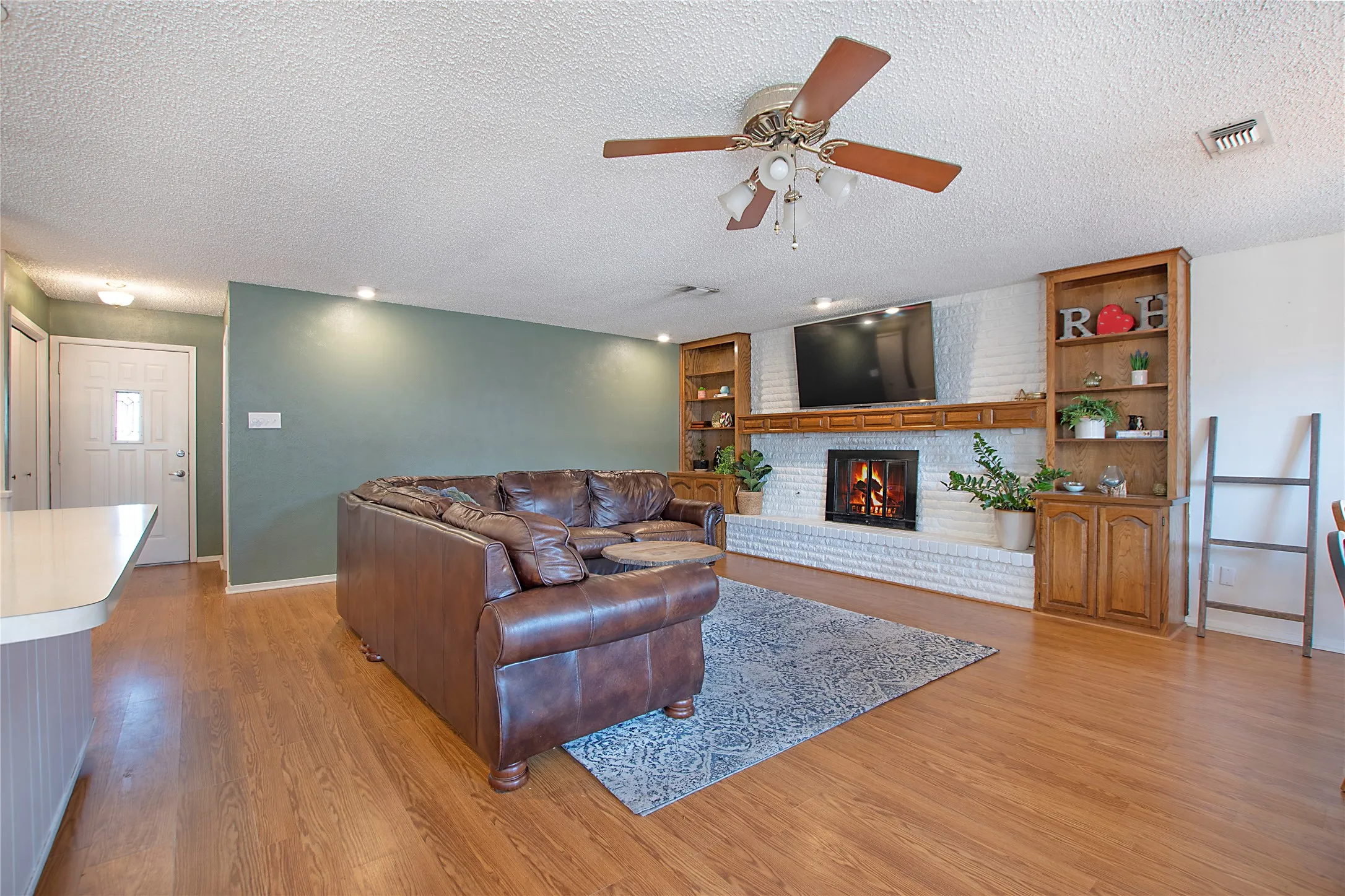 Living area featuring a white brick fireplace with a wood mantle, built-in shelving, wood-finish flooring, recessed lighting, and a ceiling fan