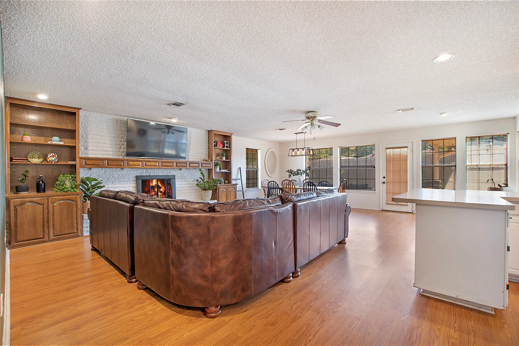 Spacious living area featuring wood-finish flooring, a white brick fireplace with a wood mantel, and built-in cabinetry