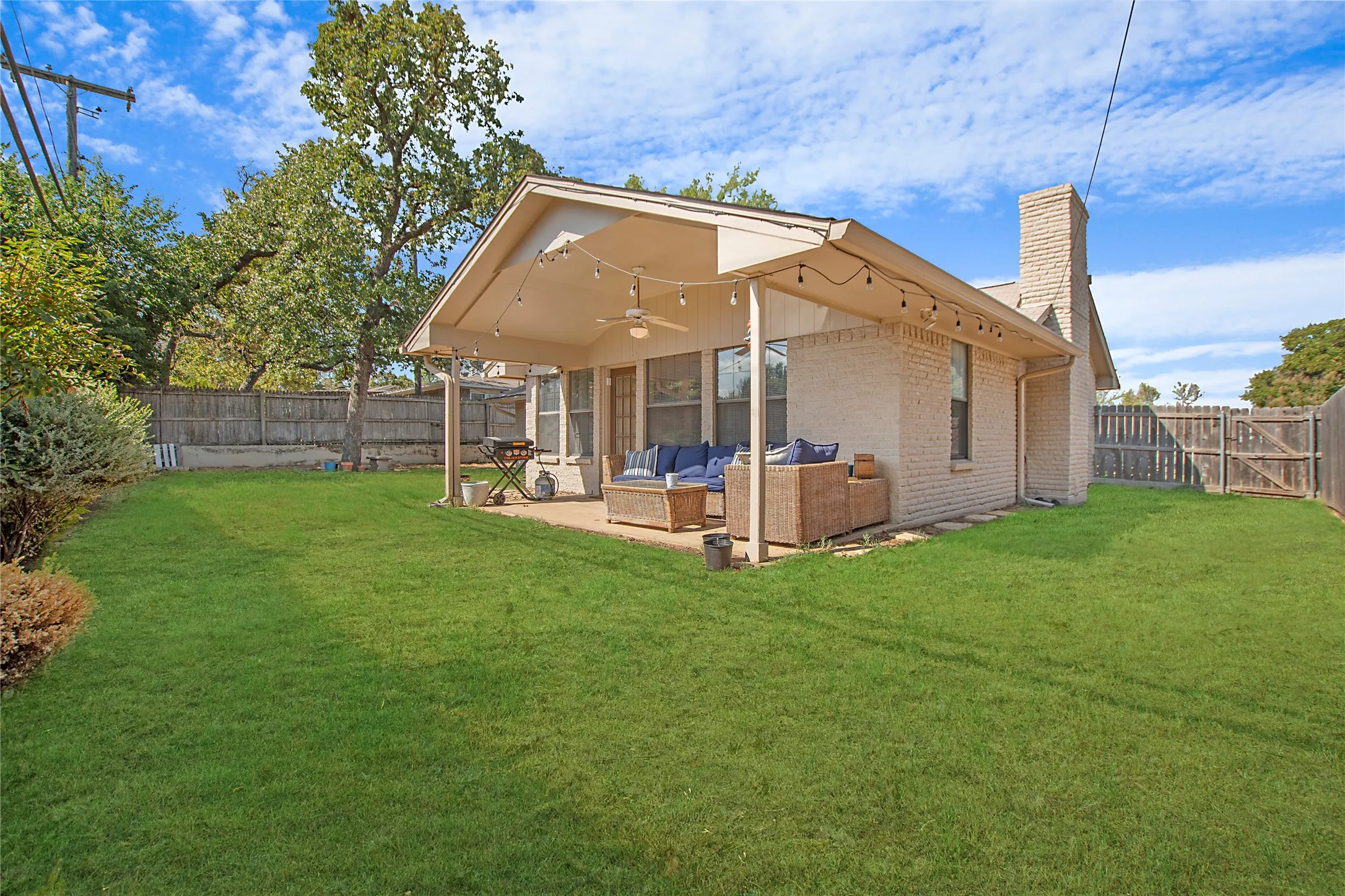 Expansive backyard featuring a covered patio, brick exterior, and a privacy fence