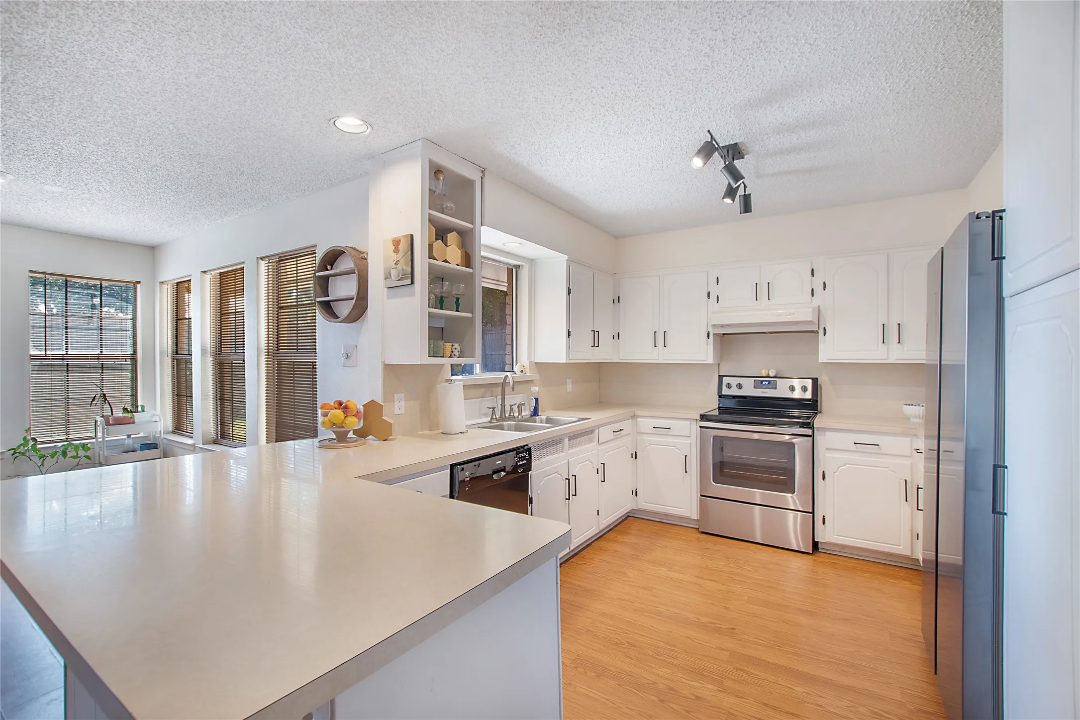 Kitchen featuring a U-shaped countertop, white cabinetry with silver-toned hardware, stainless steel appliances, wood-finish flooring, and multiple windows