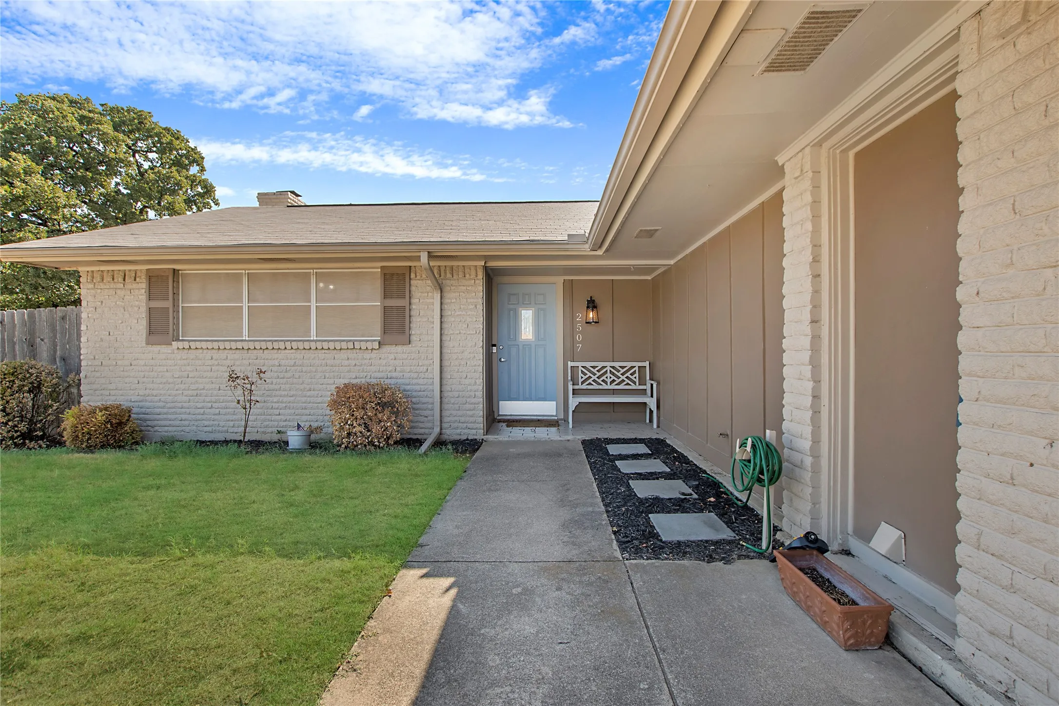 Brick exterior featuring a light blue entry door, concrete walkway, and landscaped front yard with decorative stepping stones