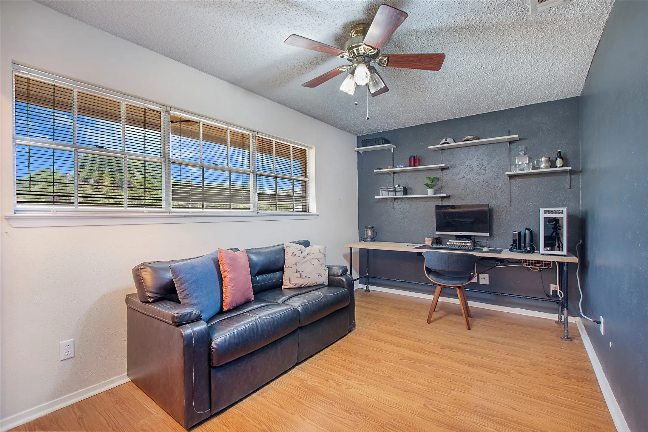 Bright room featuring wood-finish flooring, a full wall of windows with blinds, and a ceiling fan