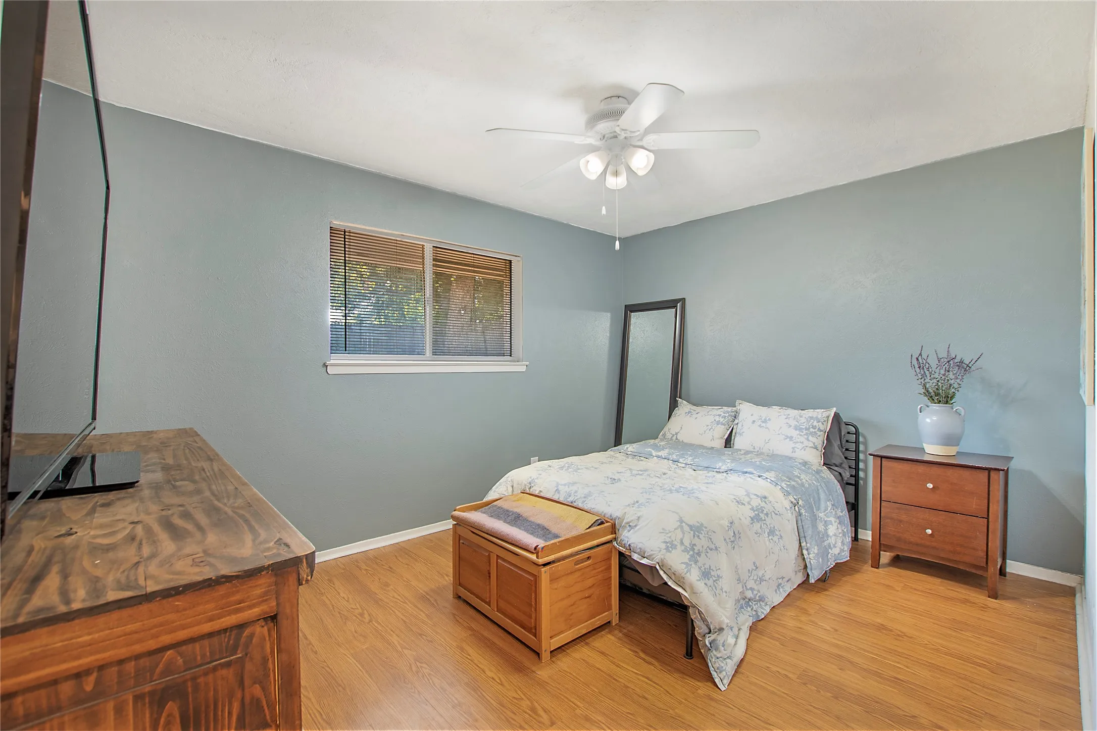 Bedroom featuring wood-finish flooring, a ceiling fan with integrated lighting, and a single window with white trim