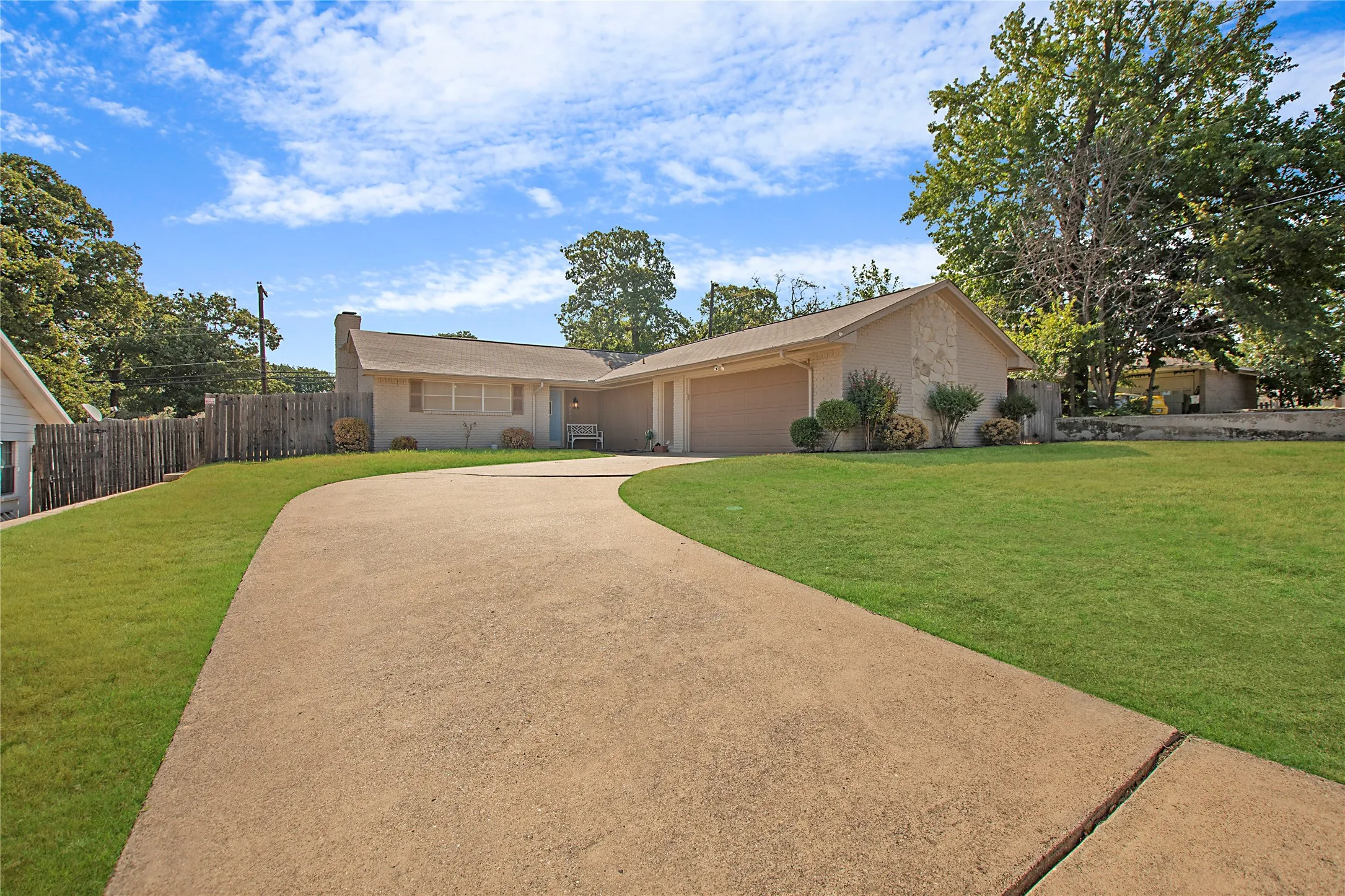 Sweeping concrete driveway leading to a tan stucco home with an attached two-car garage