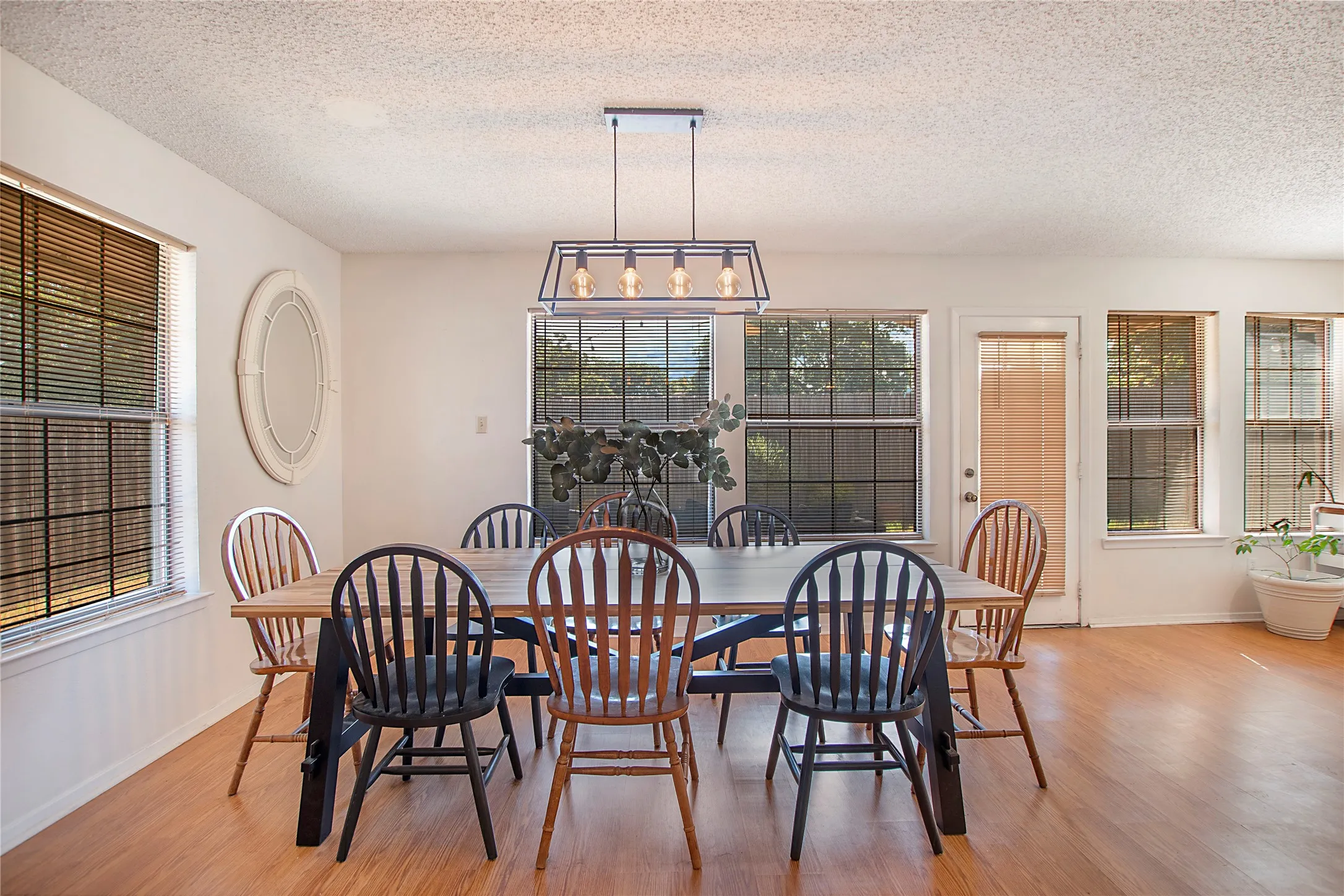 Dining space featuring wood-finish flooring, multiple windows with blinds, a white door with a window, and a linear chandelier with exposed bulbs