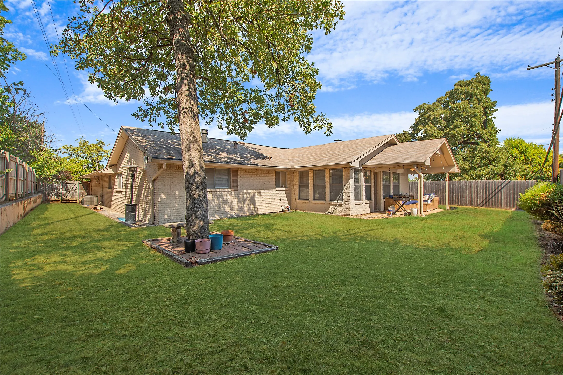 Expansive grassy backyard featuring a mature tree, brick exterior, covered patio, and wood privacy fencing