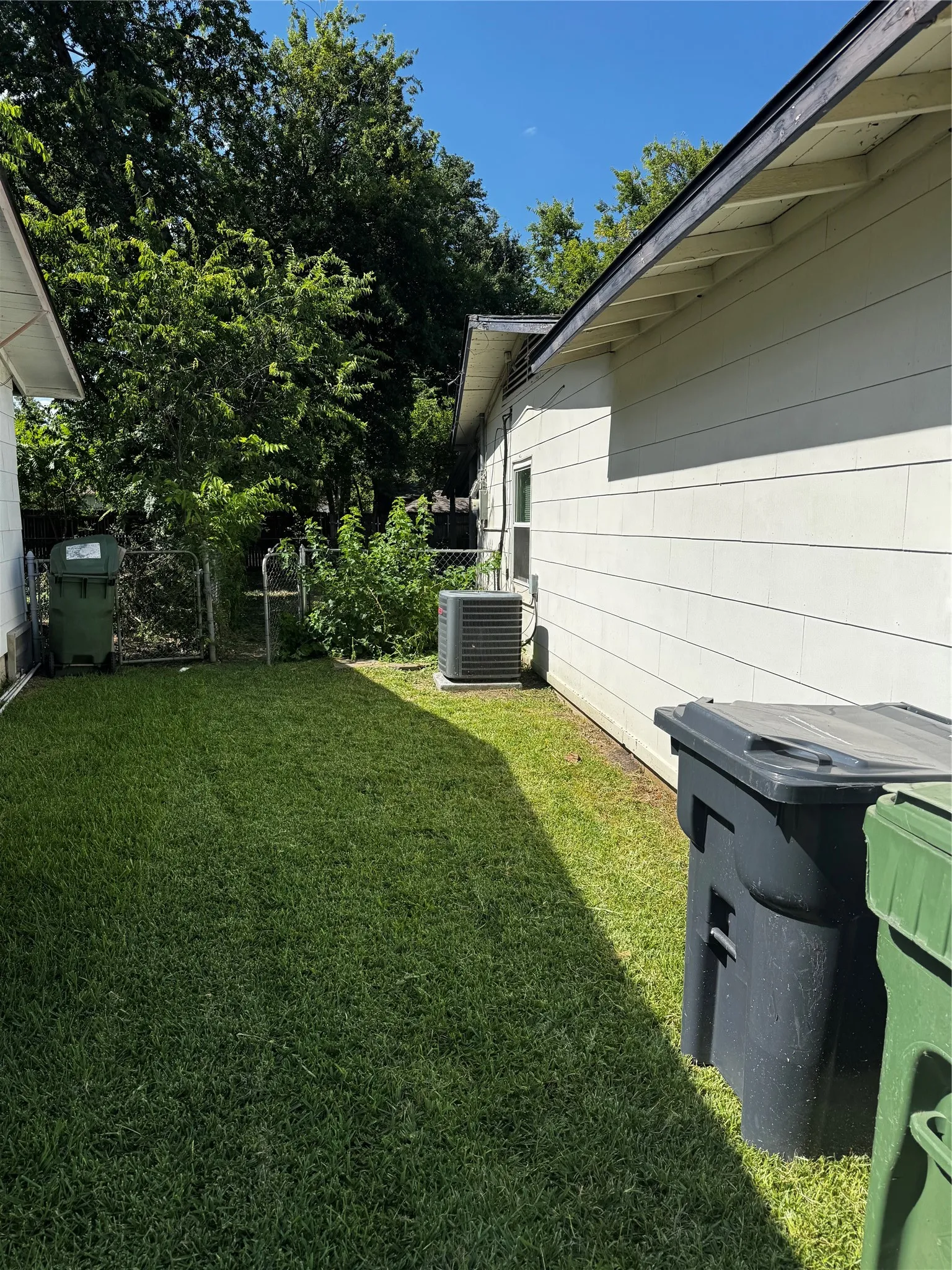 Side exterior featuring white horizontal siding, a visible air conditioning unit, and a manicured grass area